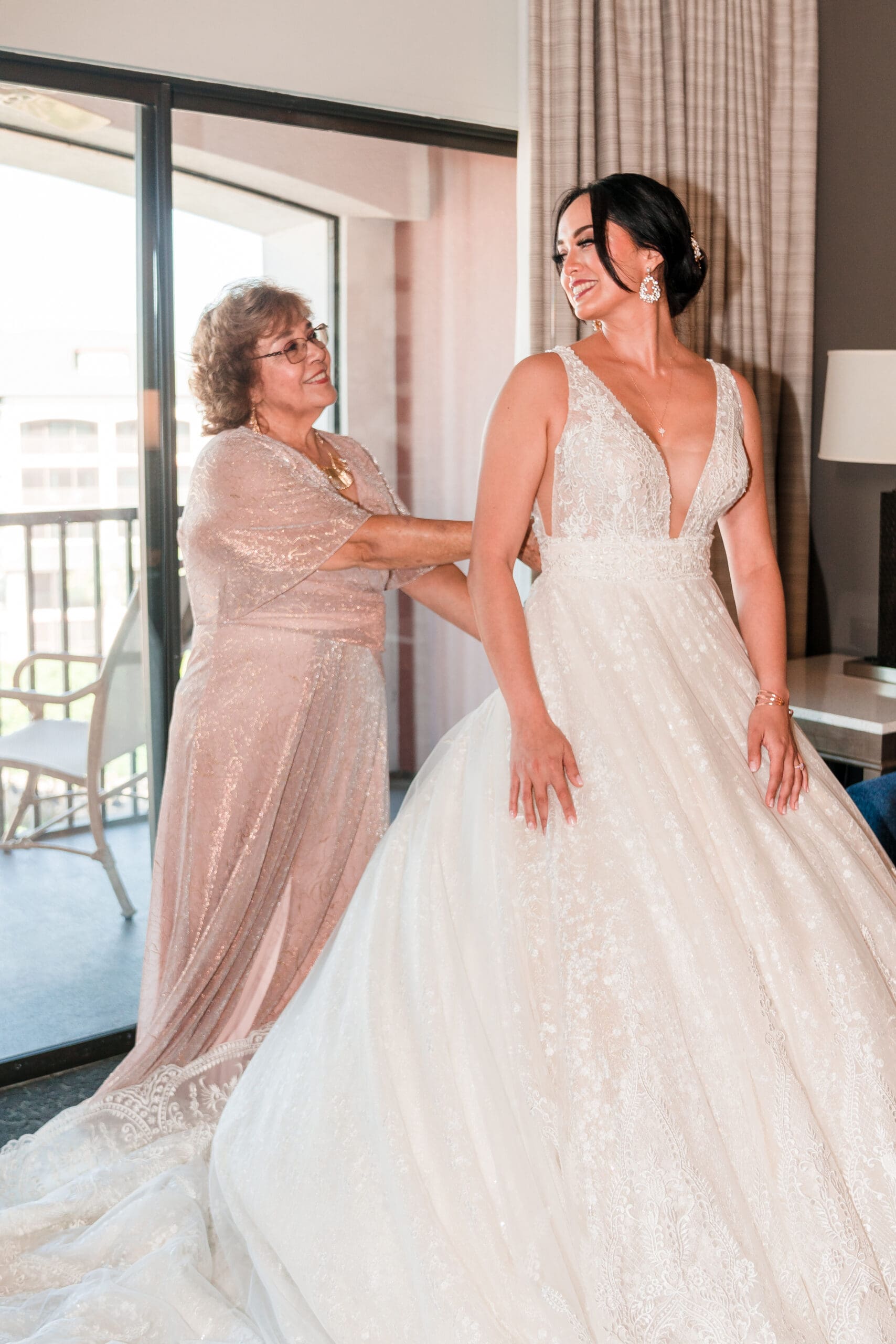 Jessica's mom zipping up her dress in the bridal suite, both smiling and looking at each other