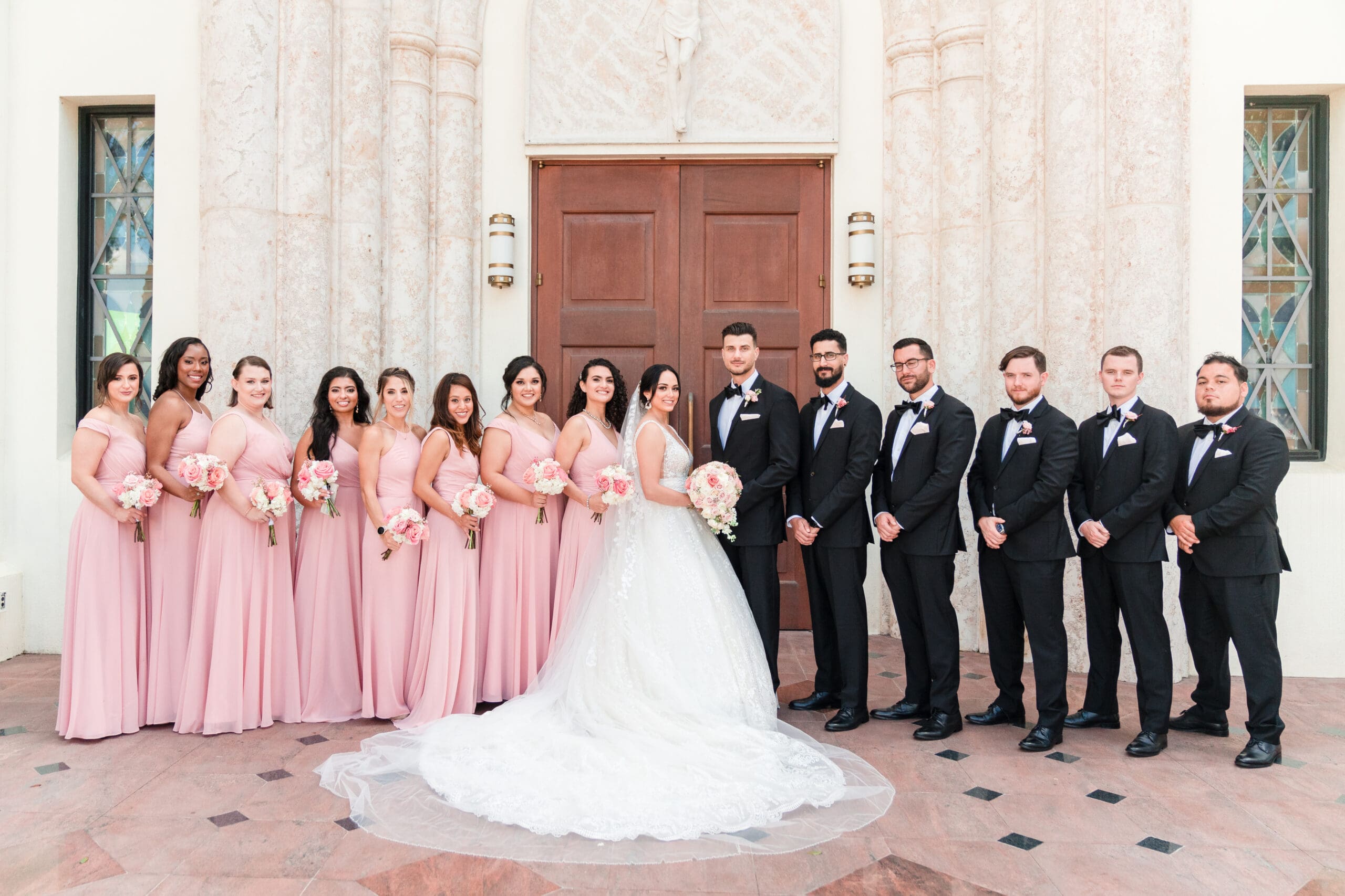 Bride and groom standing in front of St. James Cathedral with bridesmaids and groomsmen behind them, capturing a joyous moment of unity.