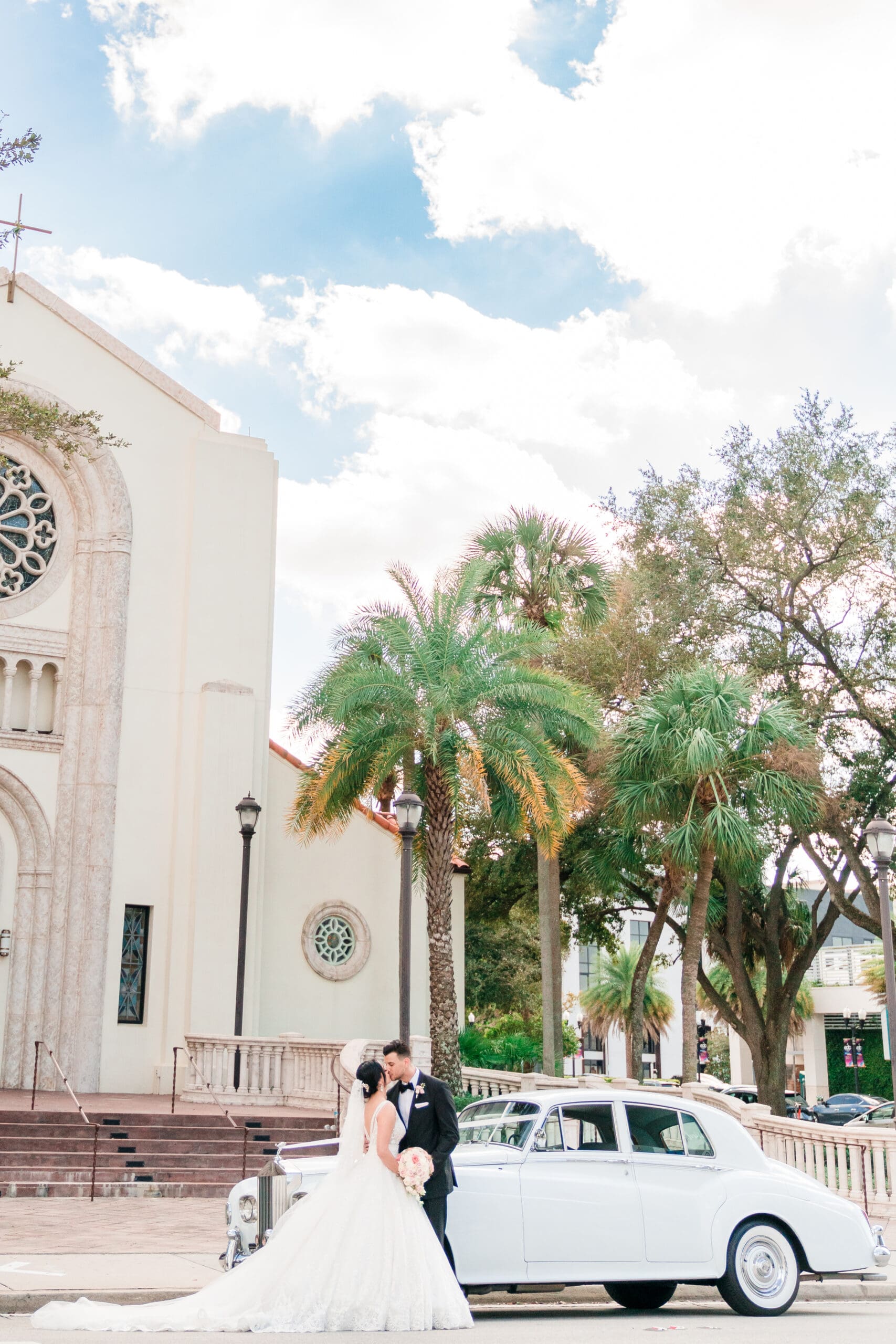 Tall shot capturing Jessica and Javier kissing in front of their car, with St. James Cathedral in the background.