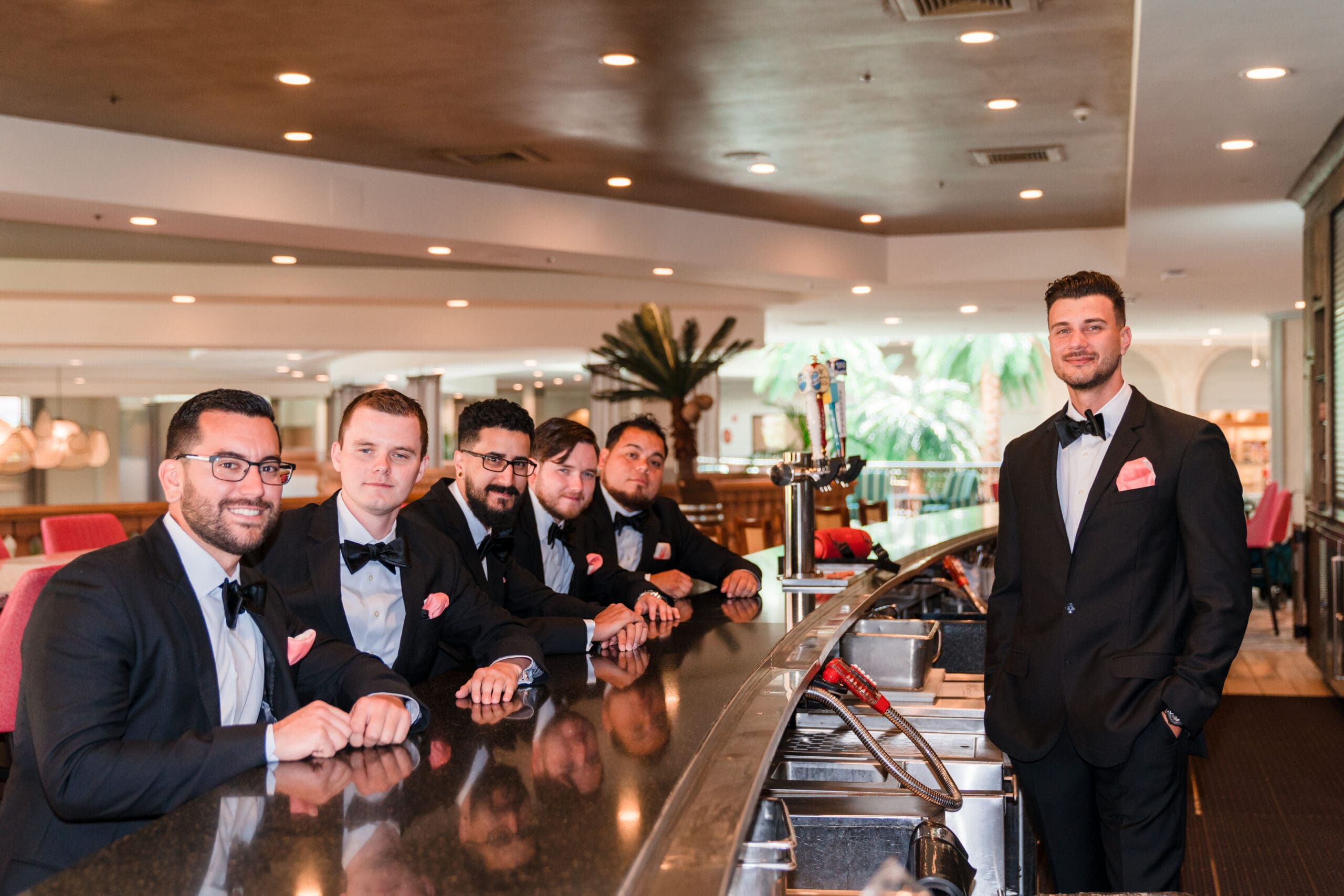 Javier and his groomsmen behind the bar at Caribe Royale Orlando, all wearing matching tuxedos with pink pocket squares.