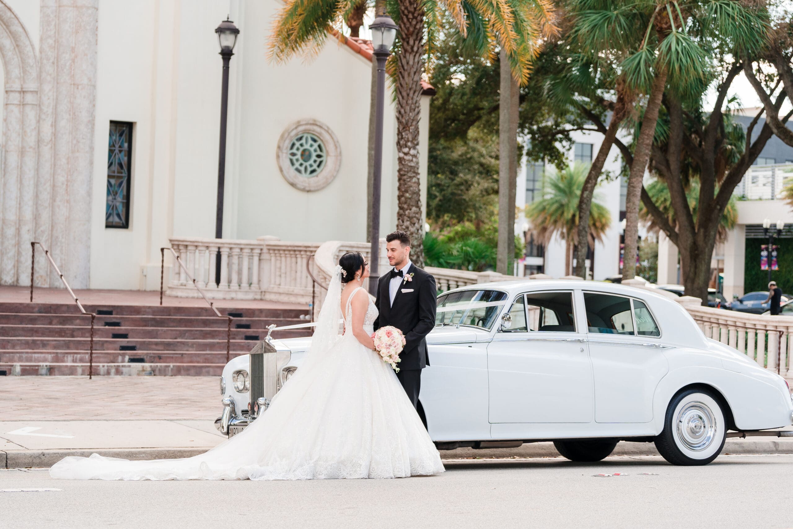 Wide shot capturing Jessica and Javier kissing in front of their car, with St. James Cathedral in the background.