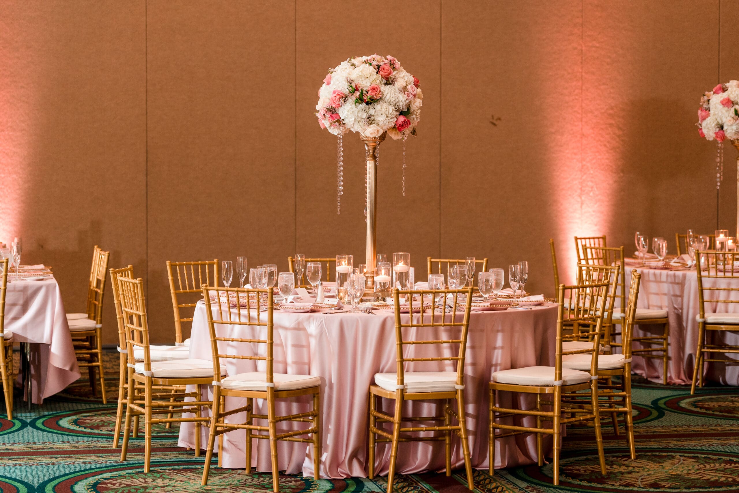 Close-up of a guest table at the Orlando Royale Caribe Reception, featuring a pink tablecloth, white rose flower centerpiece with pink roses, and elegant place settings.