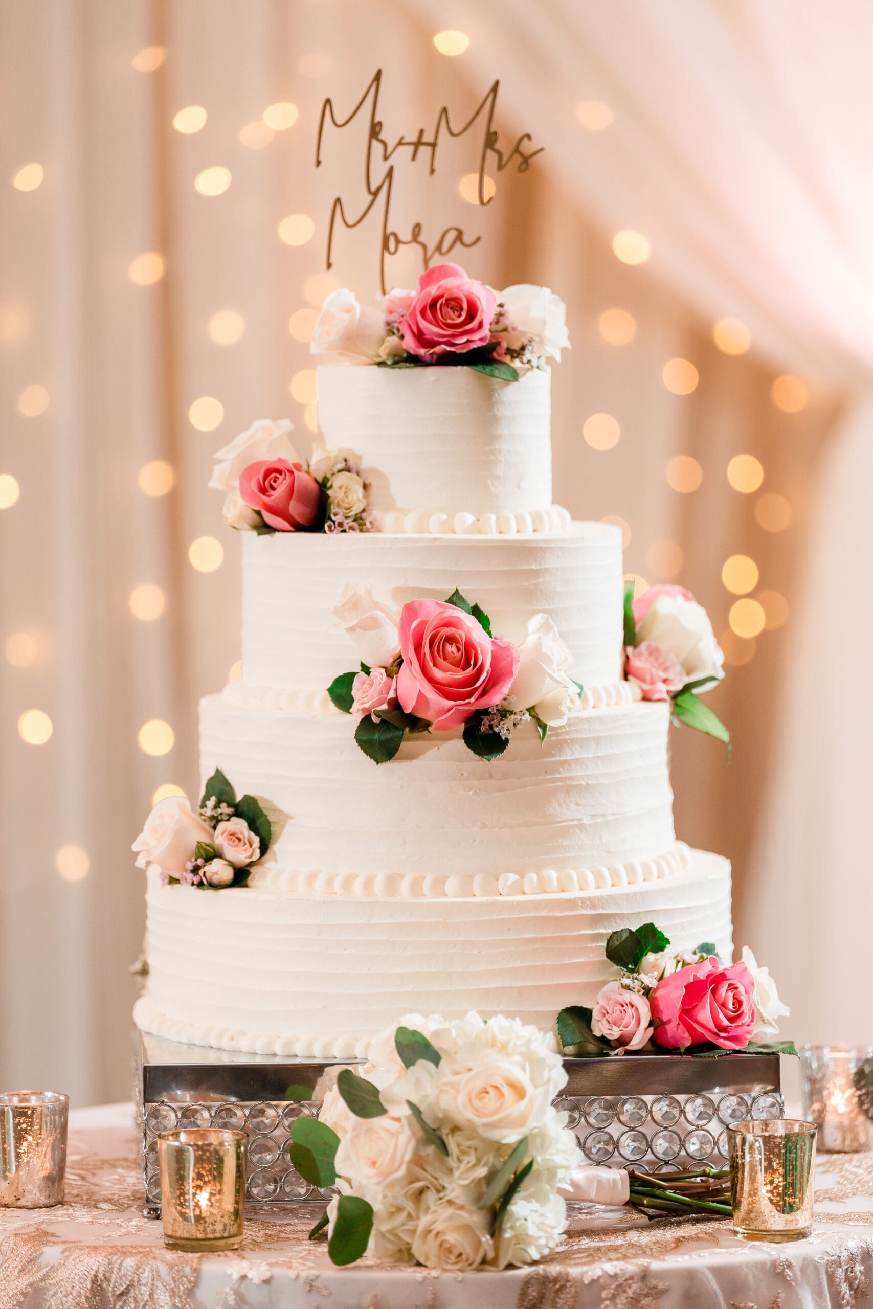 Four-tier wedding cake adorned with red and white edible flowers