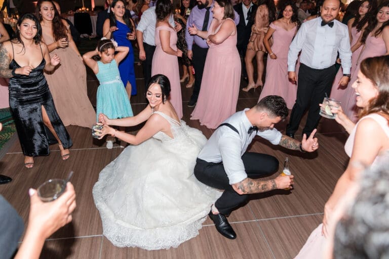 Javier and Jessica on the dance floor, touching butts while holding drinks, surrounded by friends and family laughing in joy at the Orlando Royale Caribe reception center, captured by Jerzy Nieves Photography