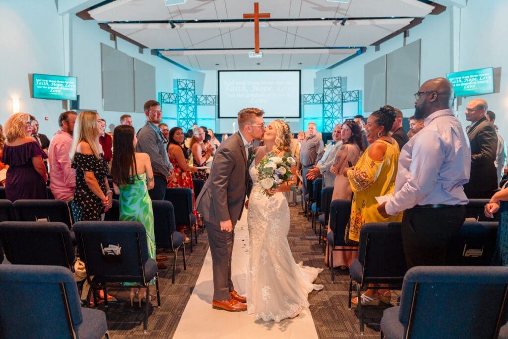 Preston and Delisa sharing a kiss midway down the aisle with friends and family smiling around them