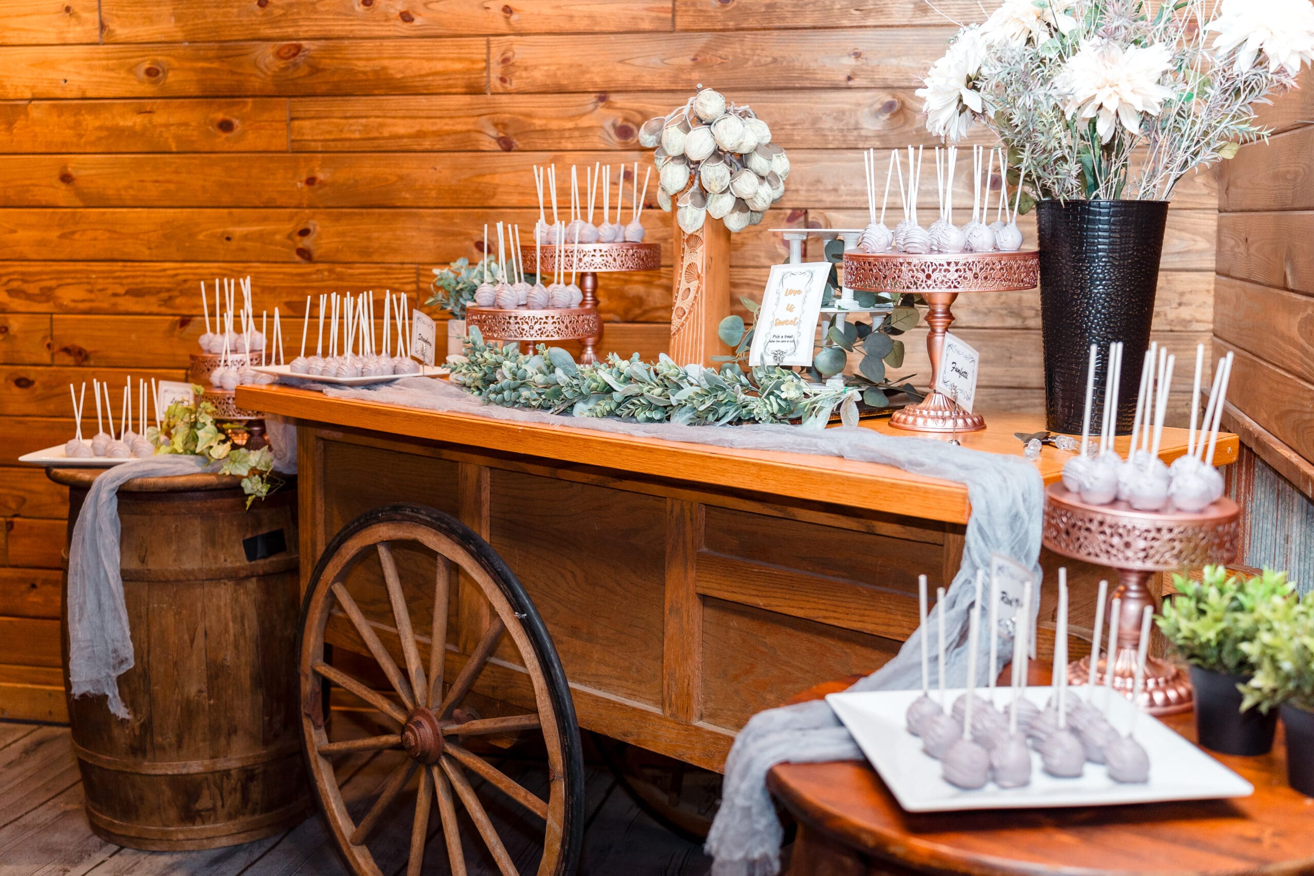 Decorative wooden wagon and barrels displaying cake pops at Hidden Barn wedding
