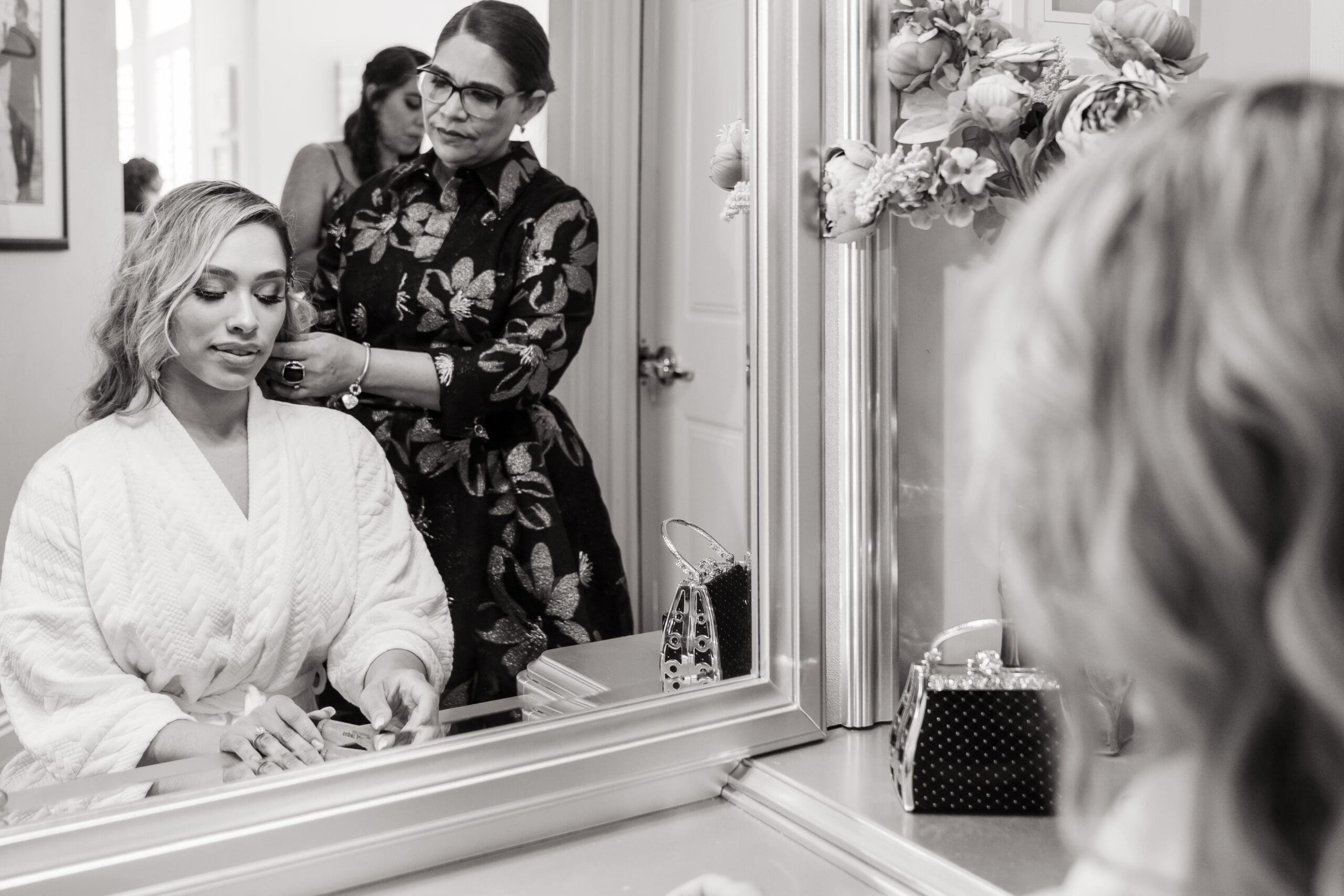 Mother of the bride fixing Jenn's hair in front of the mirror in black and white