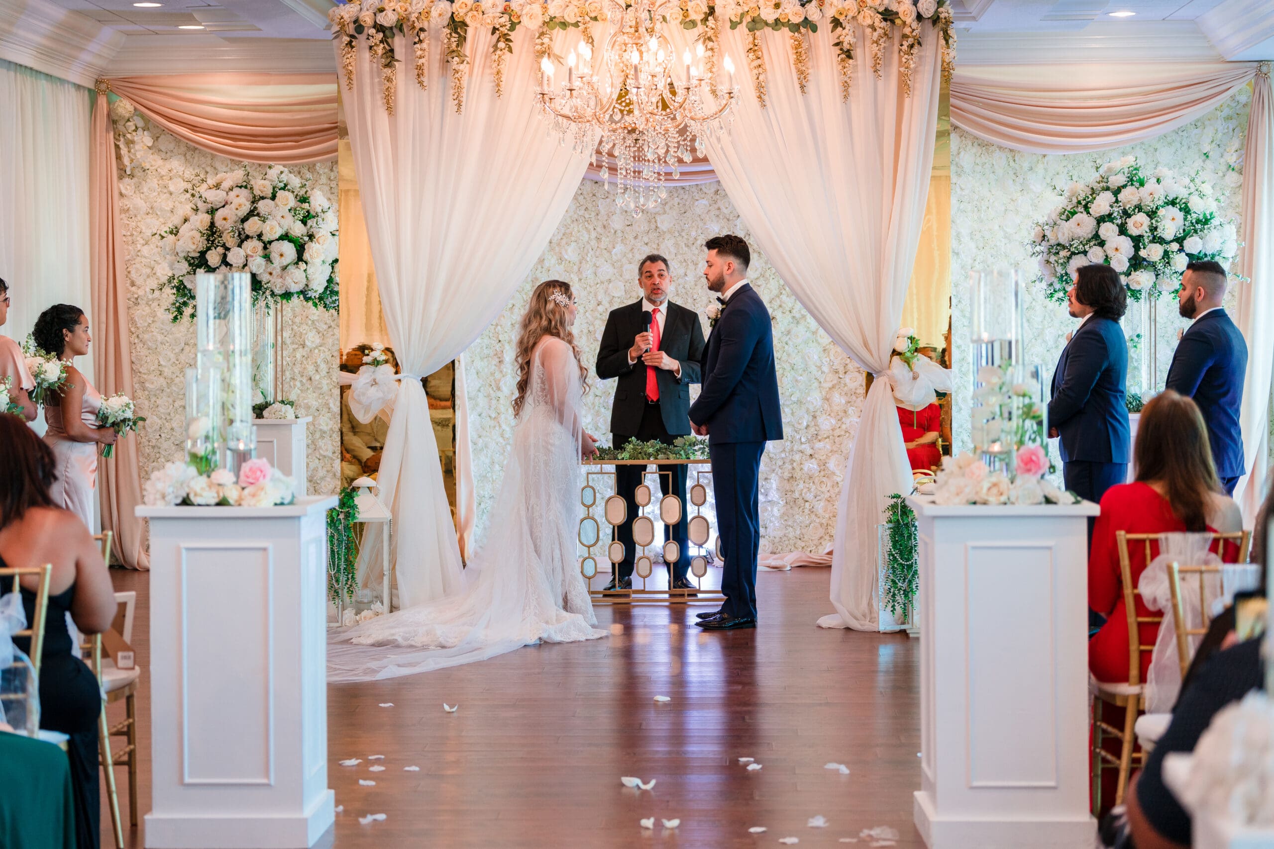 Jenn and Jazer exchanging vows at the altar amidst white drapes and roses, Crystal Ballroom Sunset Harbor.