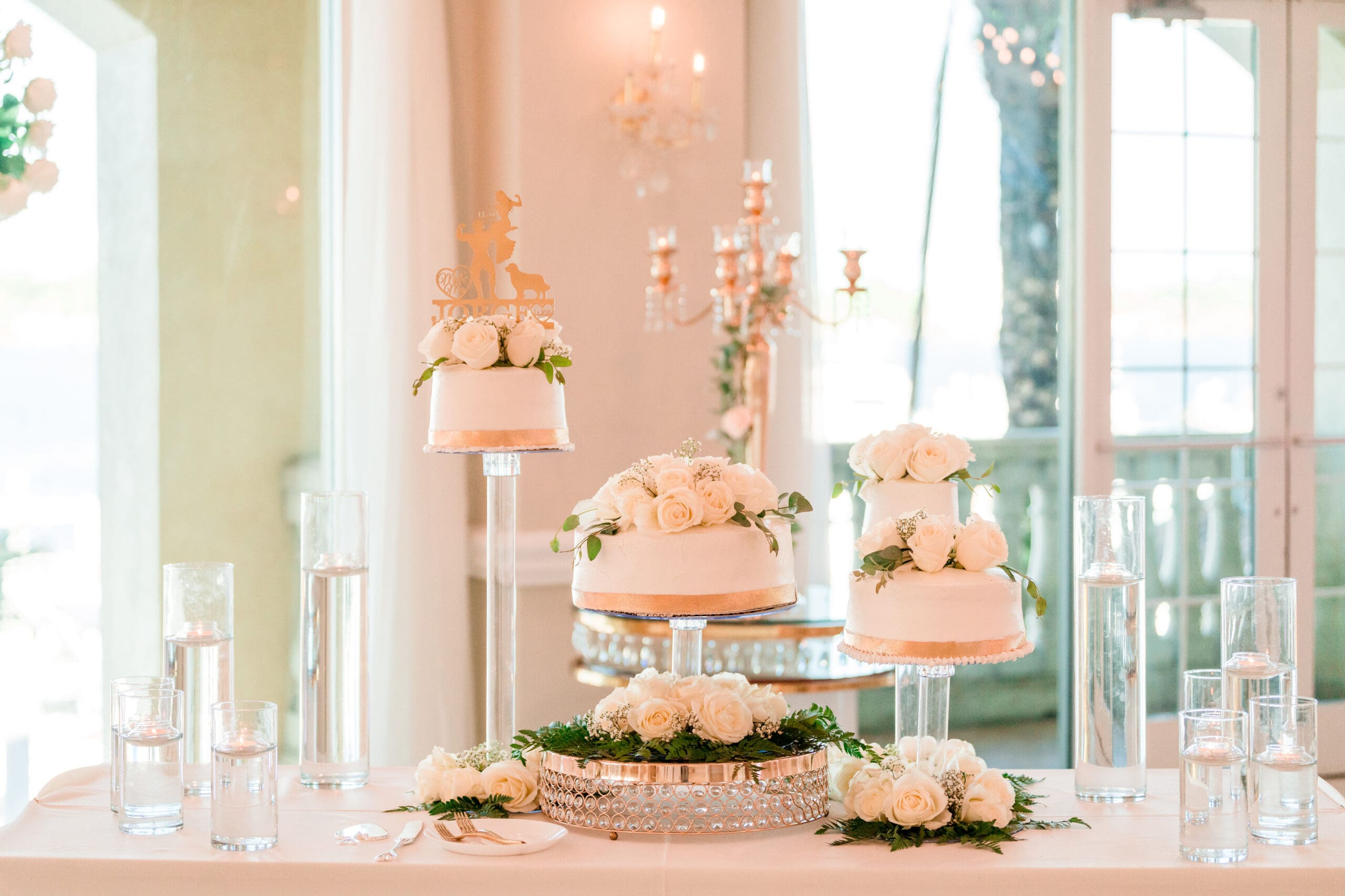 Wedding cake adorned with white edible flowers on multiple tiers, displayed on a table with a pink tablecloth