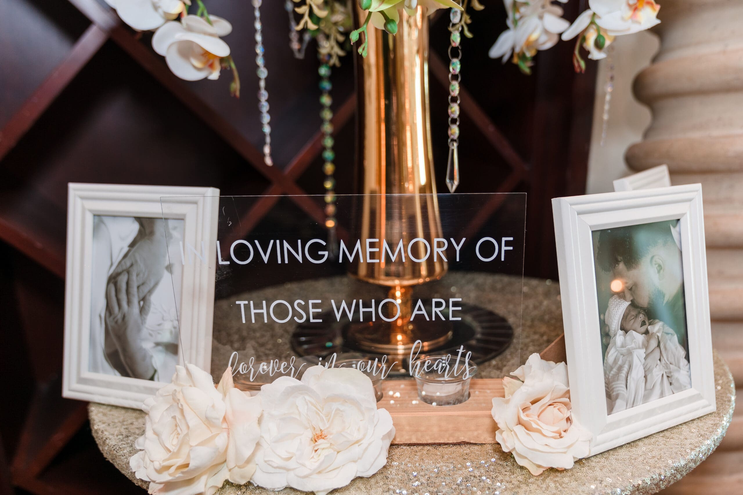 Close-up of flowers and photos with the words "In Loving Memory Of Those Who Are Here in our hearts" at Jenn and Jazer's wedding.