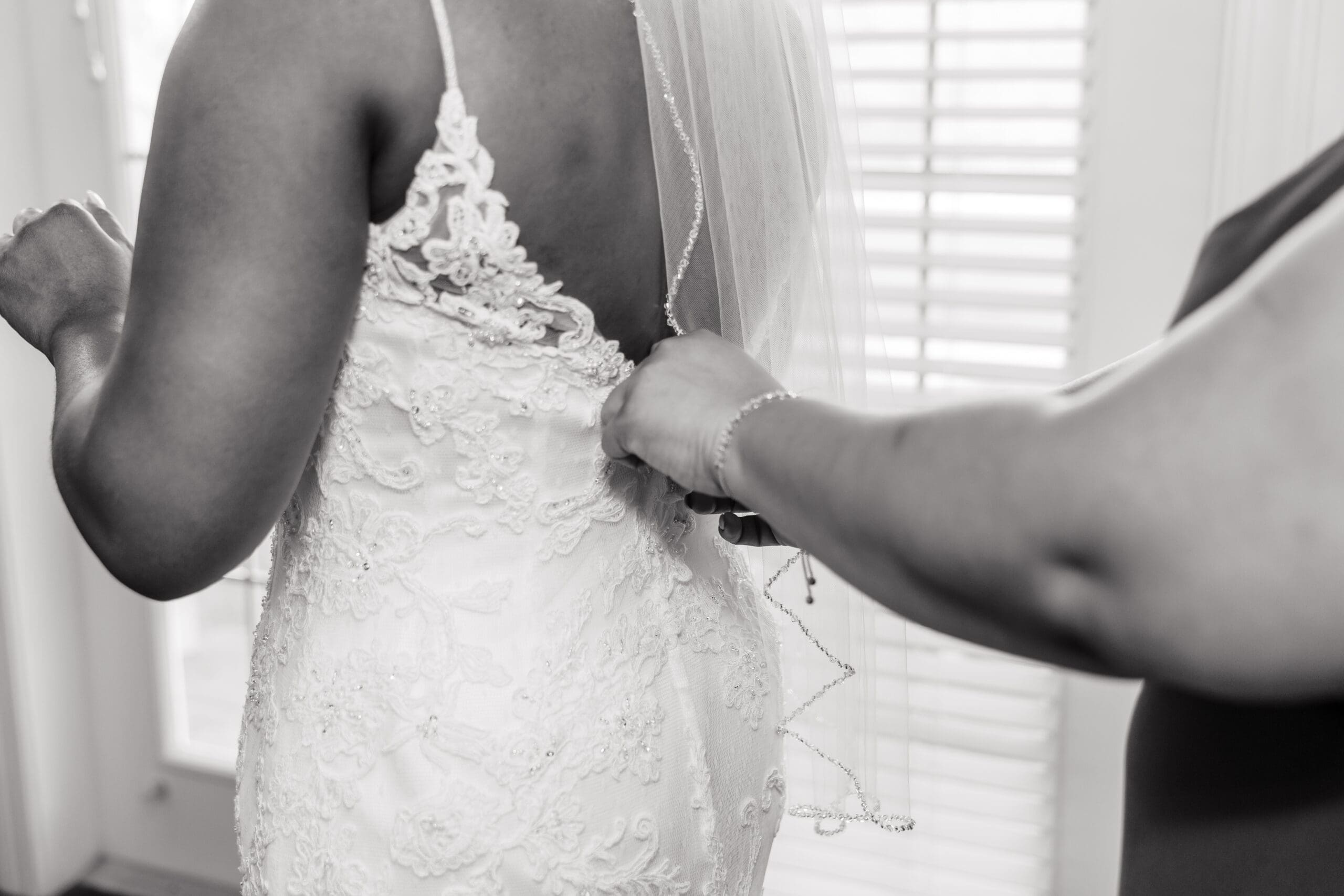 Close-up black and white shot of a bridesmaid zipping up Kourtni's dress.