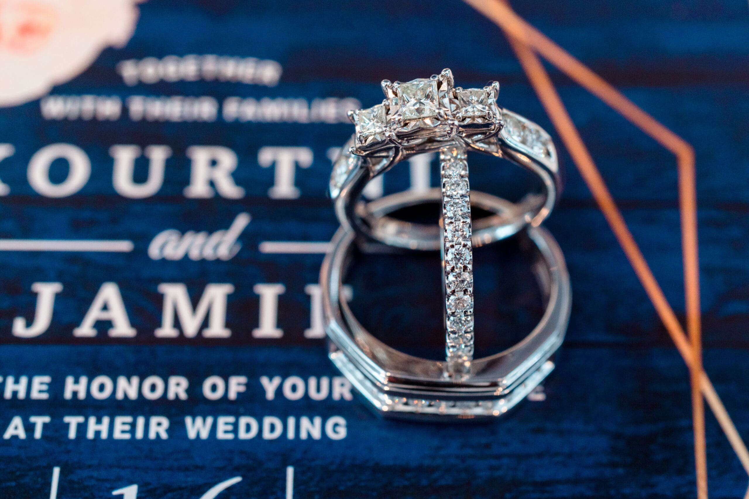 Close-up of the engagement ring and wedding bands displayed on the wedding invitation.