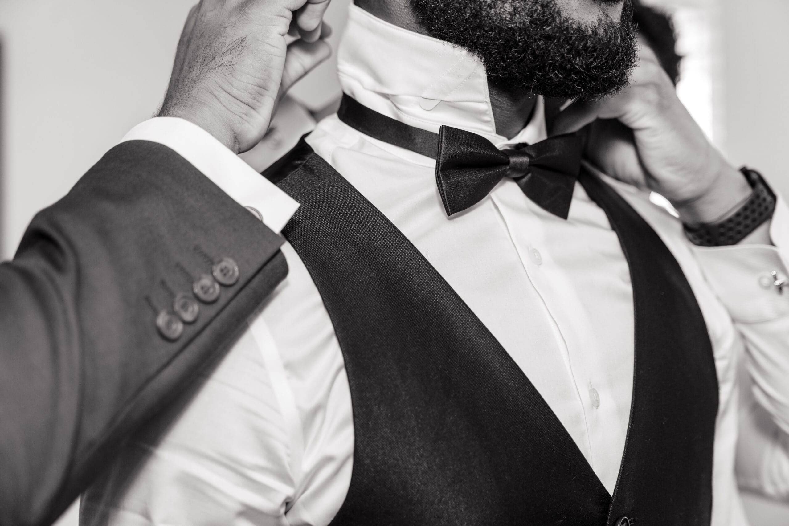 Black and White: Close-up shot of a groomsman helping the groom fix his tie and collar before the wedding.