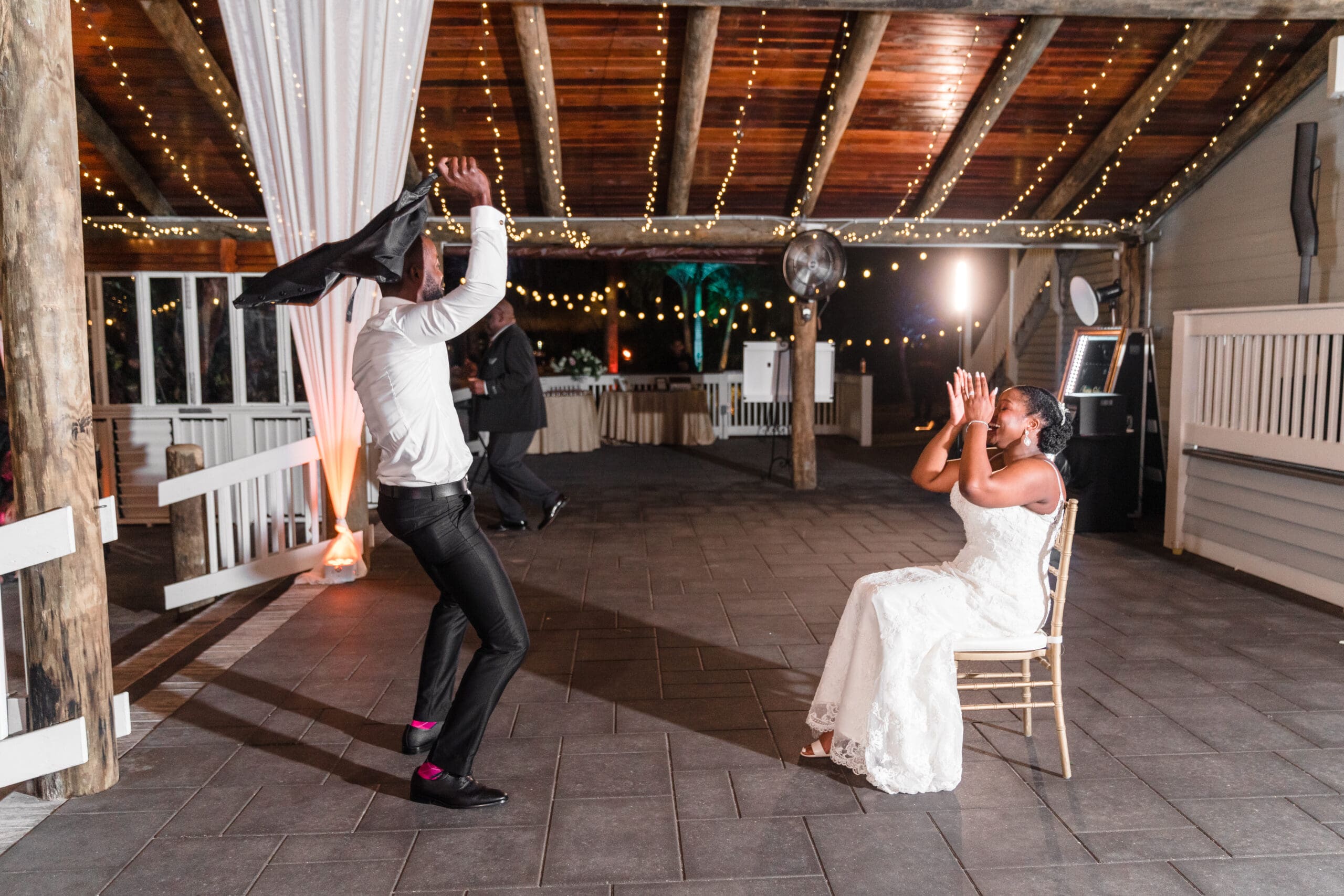 Jamie dancing for Kourtni while she sits, laughing and smiling, as he spins his sports jacket over his head in a dance, captured by Jerzy Nieves Photography.