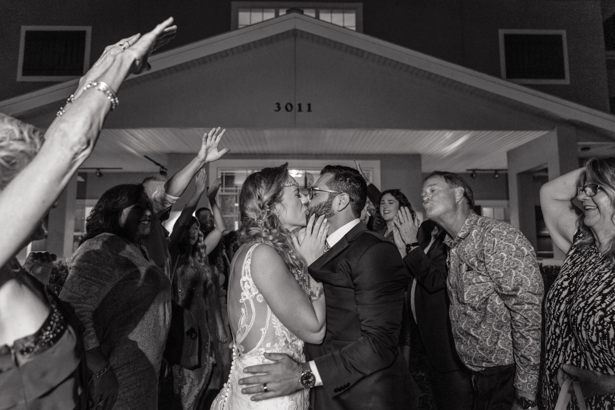 Black and white photo of Kristen and Carlos' grand exit outside the Island Grove Reception Center, guests cheering with hands in the air.