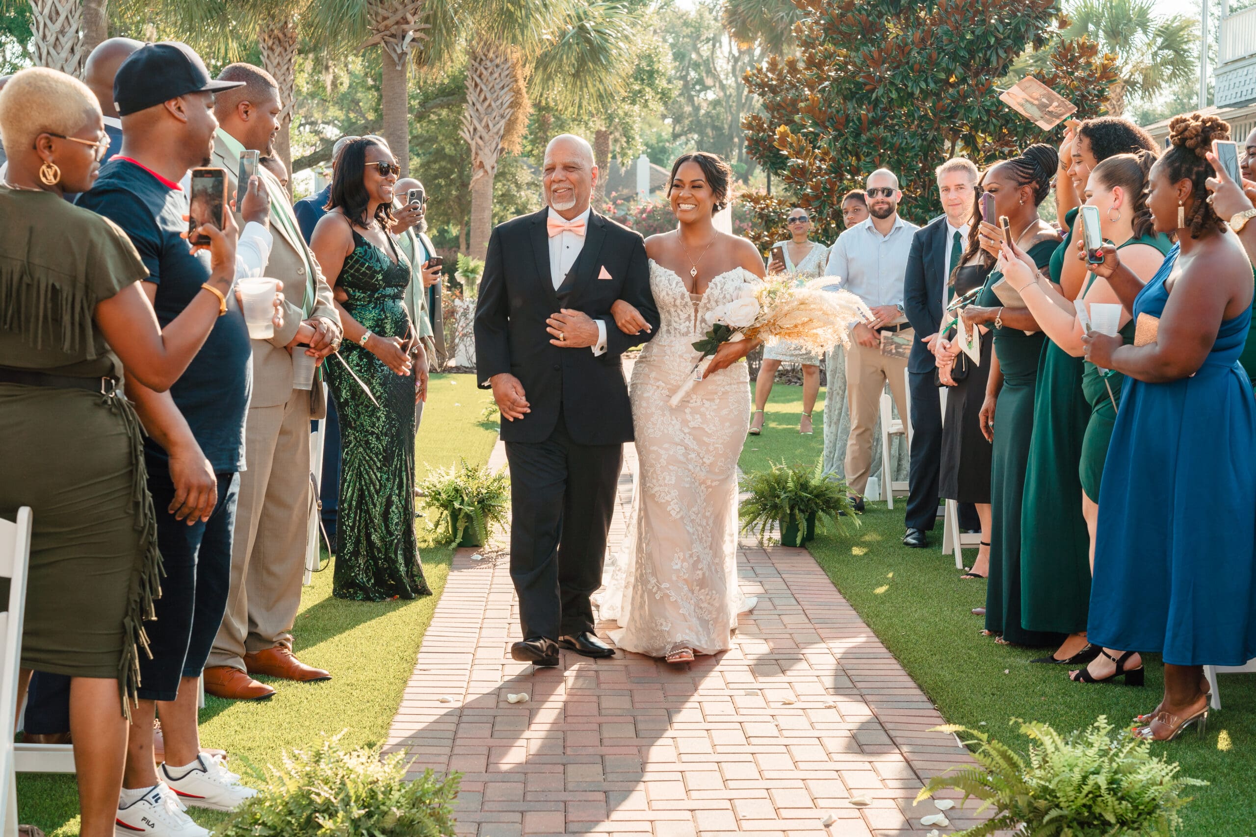 Lateisha and her father walking down the aisle towards the altar, surrounded by smiling guests taking pictures.