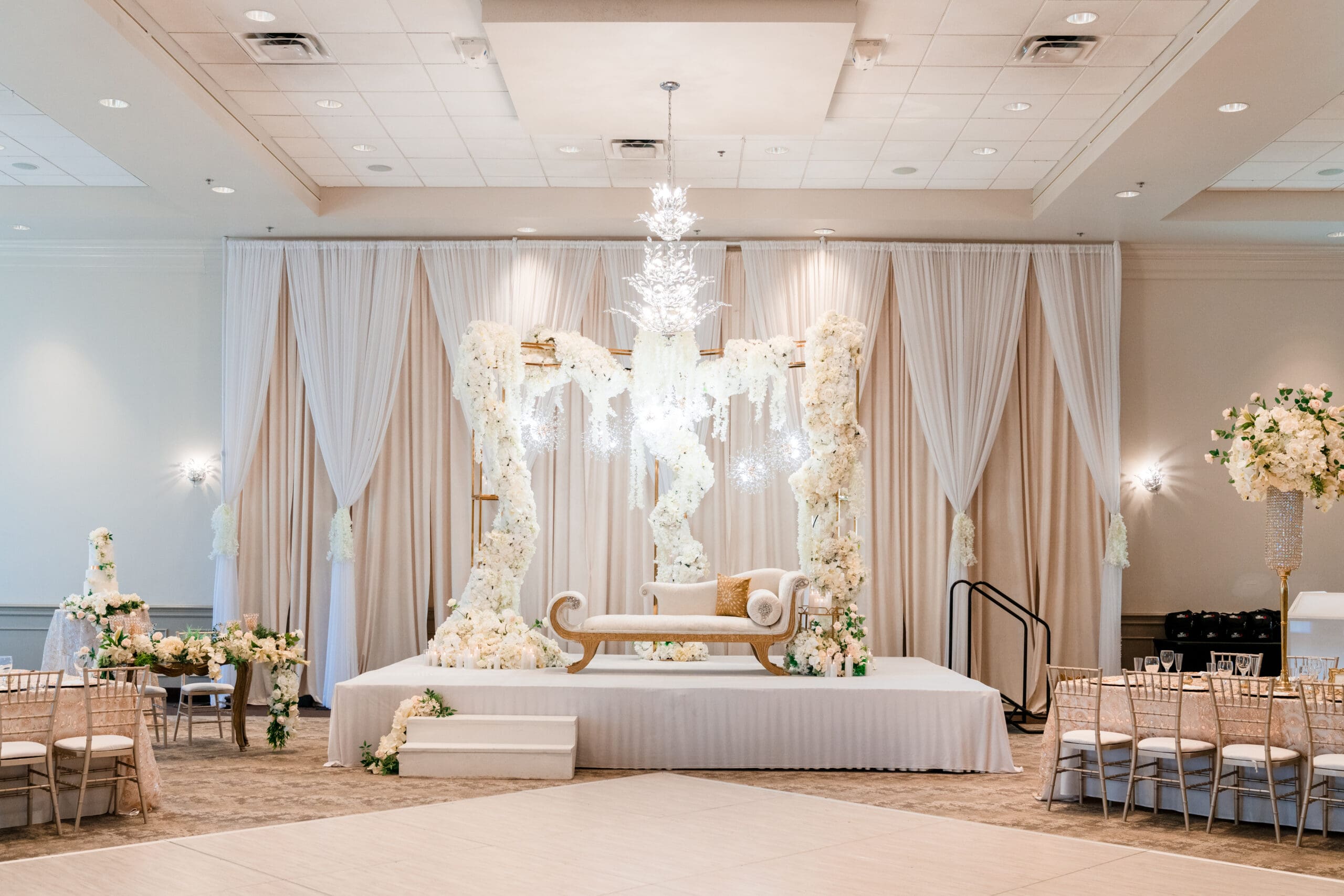 Couple's area on a stage with a white and gold elegant-looking love seat with an archway decorated with white roses at the Holy Trinity Reception Center pre-wedding
