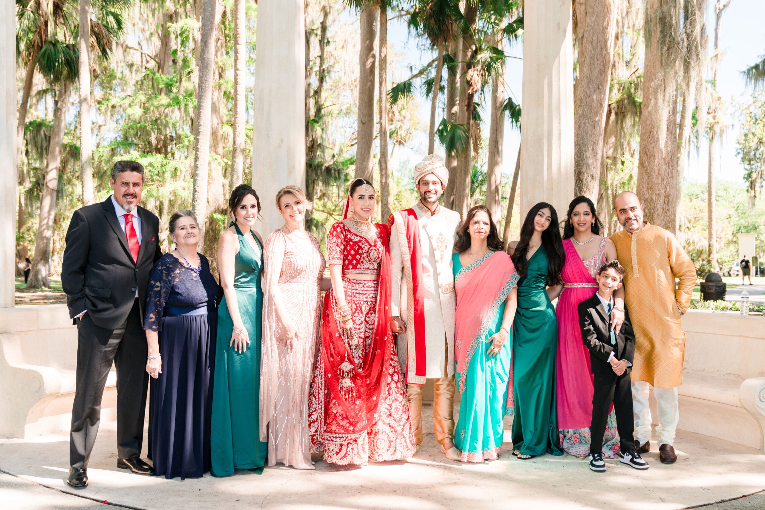Sabrina and Rahul, flanked by their families, pose in traditional Indian wedding attire alongside bridesmaids and groomsmen, at Kraft Azalea Gardens.