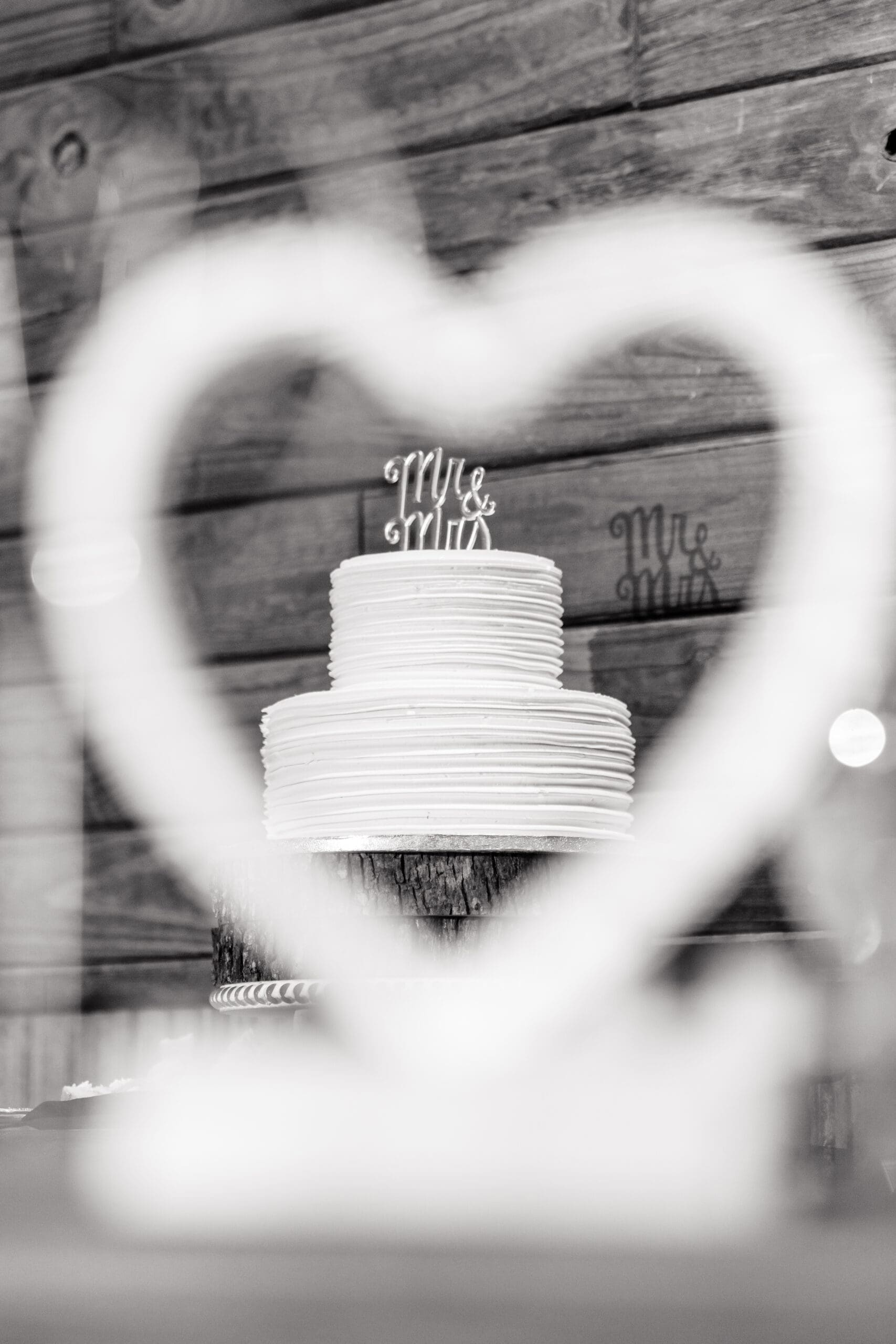 Elegant black and white tall shot of Taylor and David's wedding cake, captured through a heart-shaped table decoration