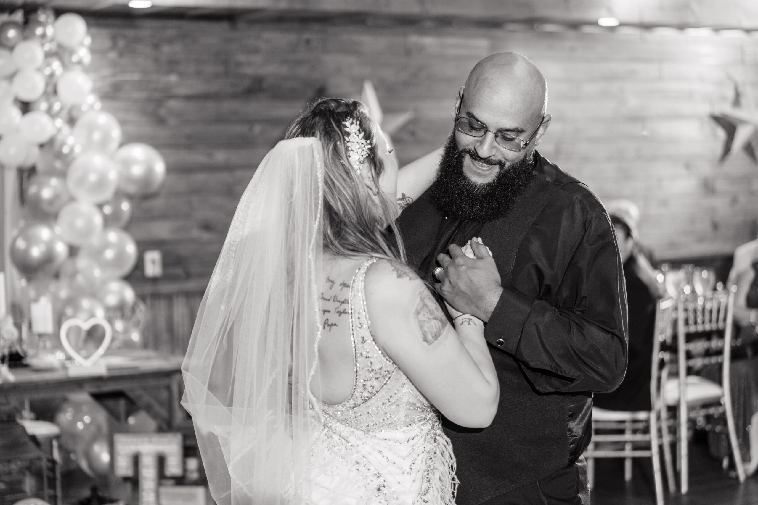 Close-up black and white shot of Taylor and David smiling as they share their first dance at the Hidden Barn
