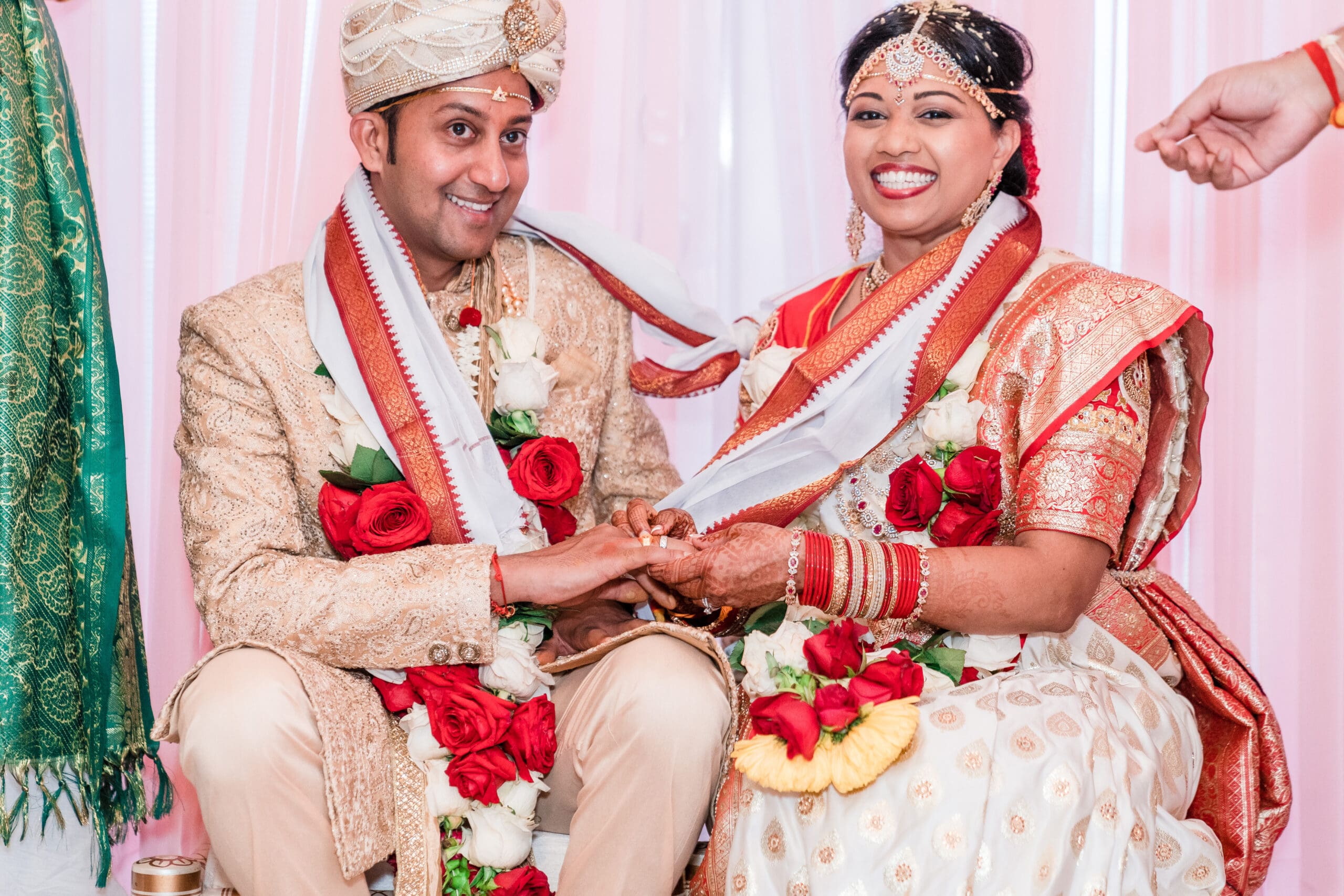 Newlywed couple in traditional Indian wedding attire embracing each other with big smiles.