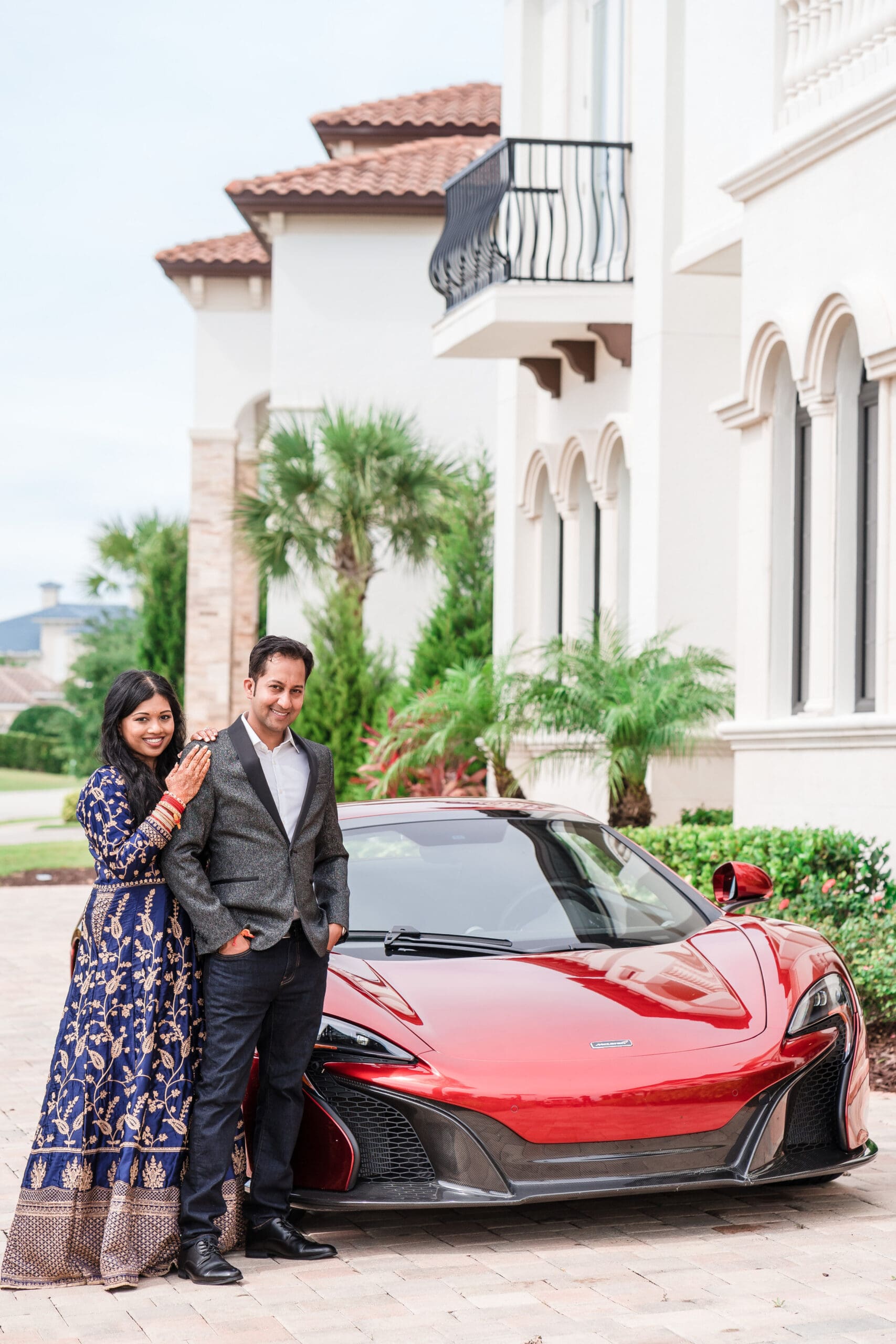 Indian wedding couple standing next to a red McLaren sports car outside the venue.