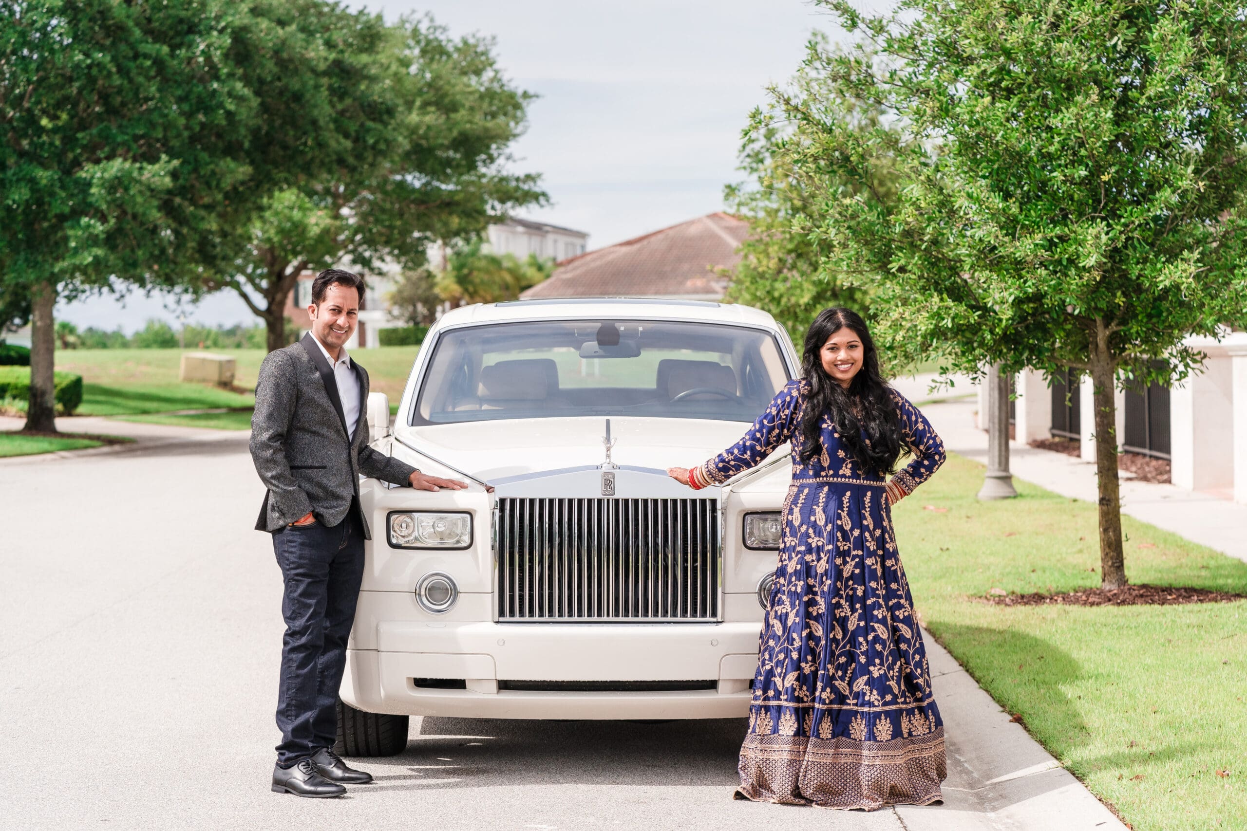 Cultural wedding couple posing on either side of their Rolls Royce vehicle for a picture.