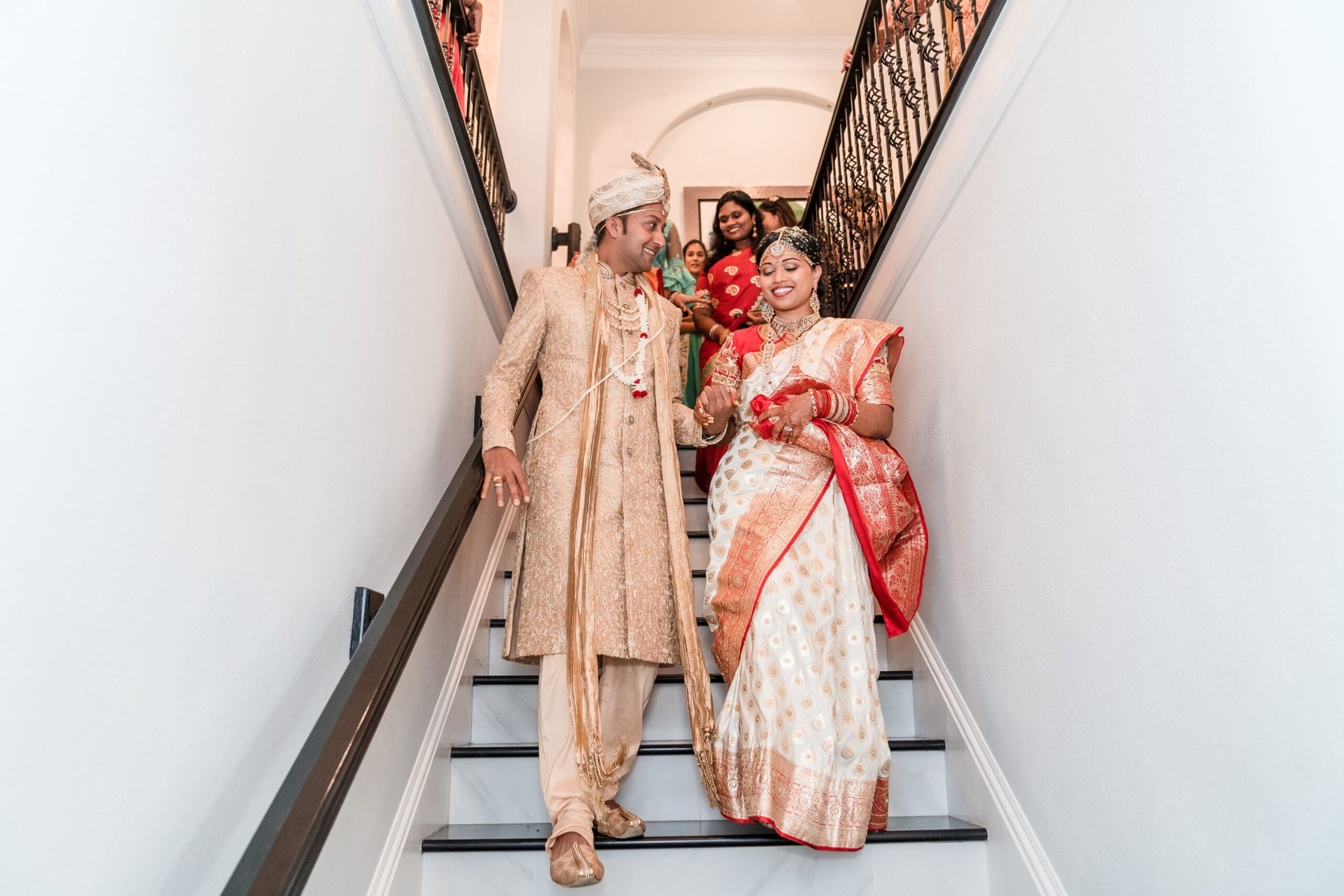 Joyful couple in traditional Indian attire holding hands while walking down stairs - cultural wedding photography