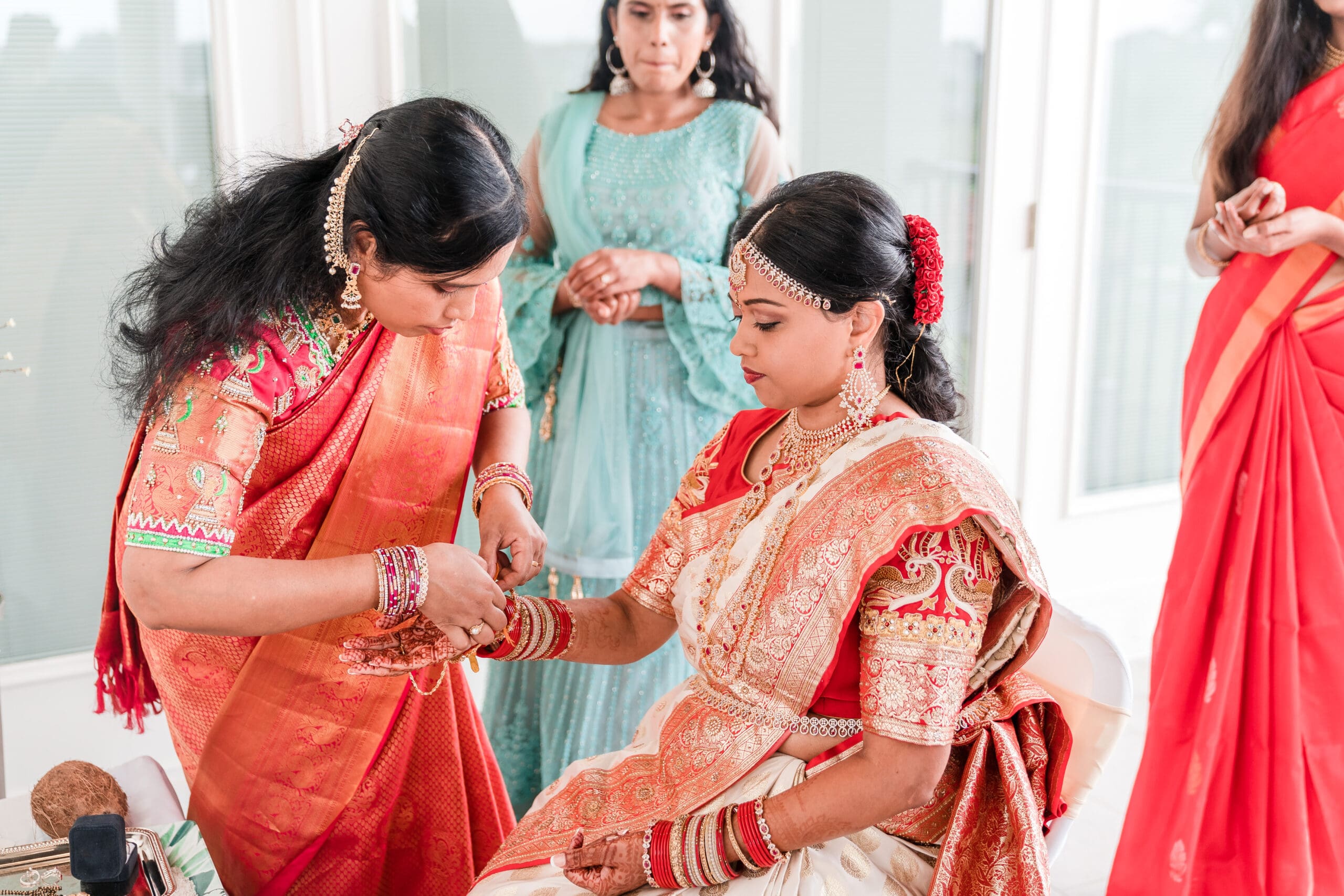Bride in traditional Indian wedding attire getting her bracelets adjusted before the ceremony.