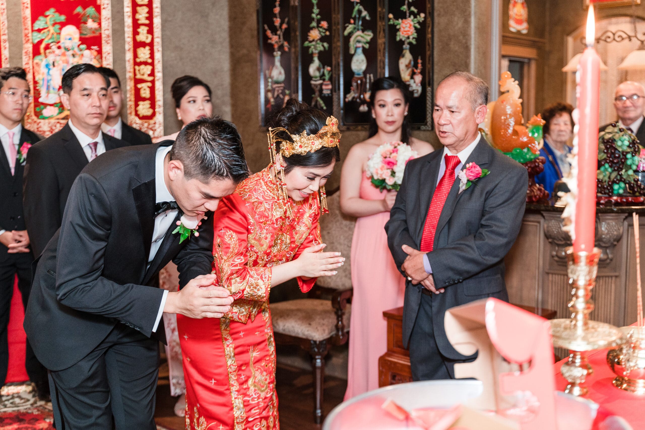 Bride and groom bowing in unison during their traditional Oriental wedding ceremony, with guests in the background