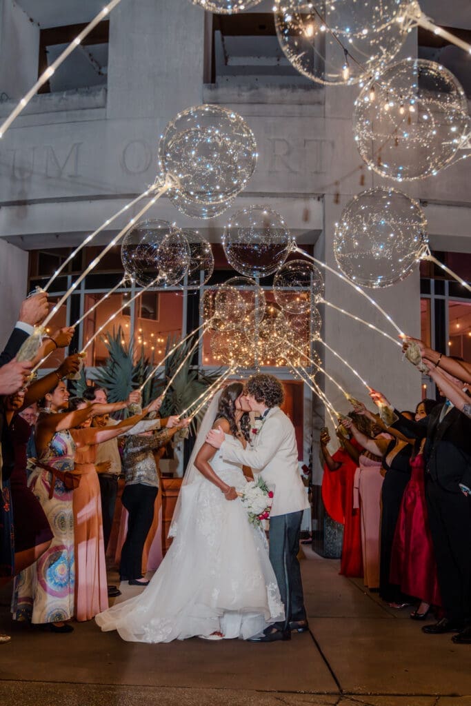 Newlyweds sharing a kiss under a canopy of glowing globe-like balloons, resembling stars