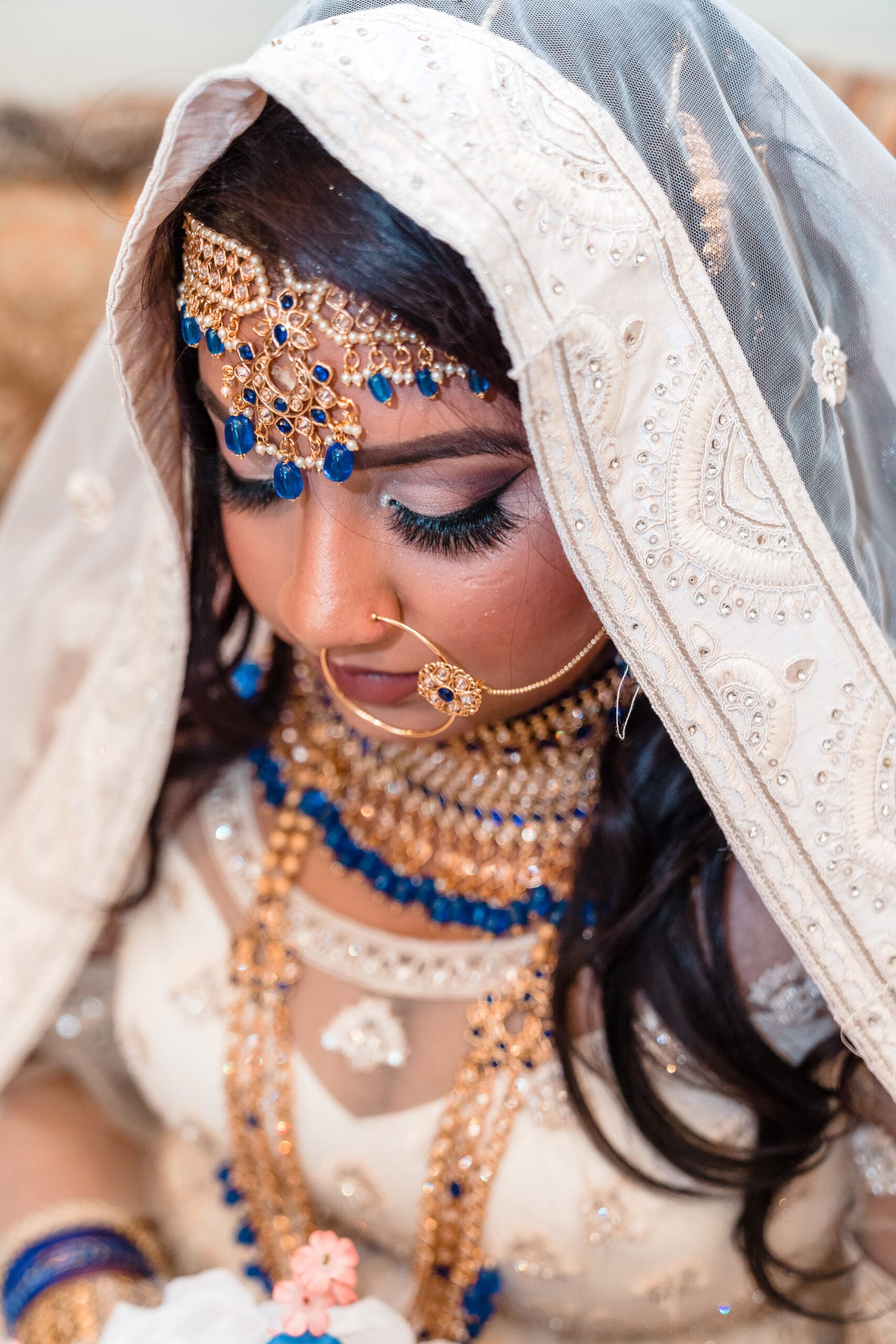 Indian bride in traditional wedding attire, wearing a white dress embellished with small jewels, adorned with intricate gold and blue jewelry