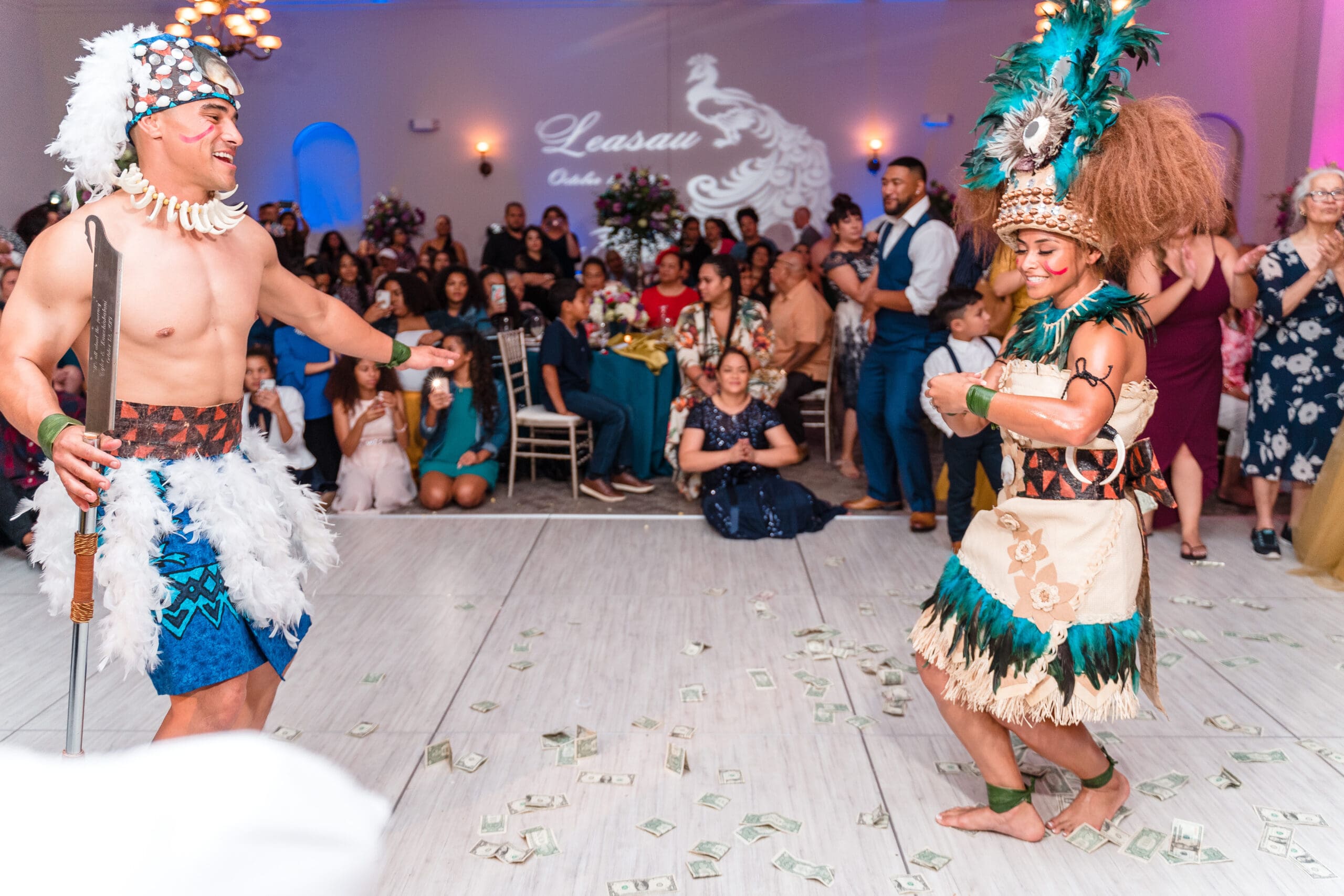 Husband and wife dressed in traditional Hawaiian wedding attire, dancing joyfully on a floor strewn with money, celebrating their union in a cultural tradition.