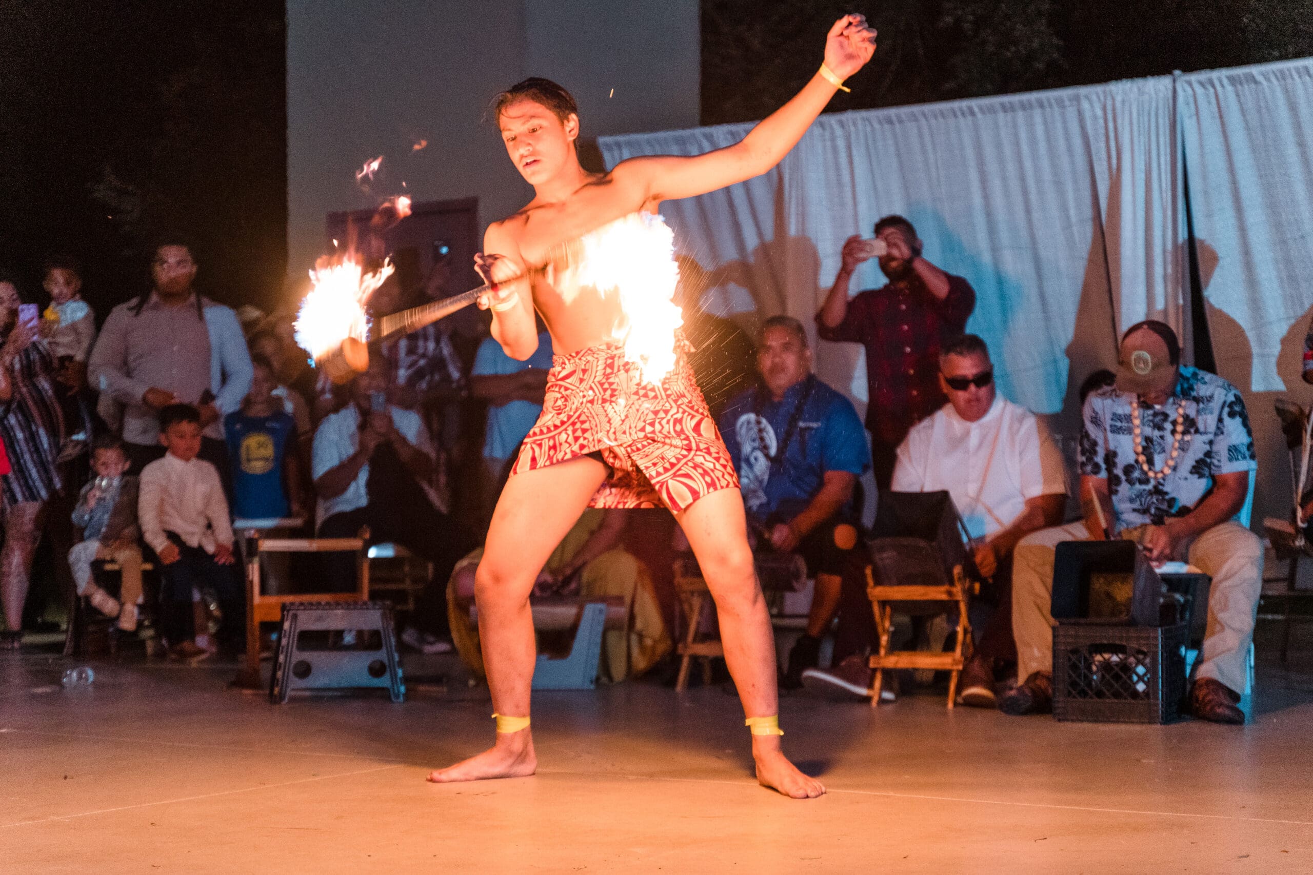 Fire twirler performing at traditional Hawaiian wedding reception, spinning flames in mesmerizing display