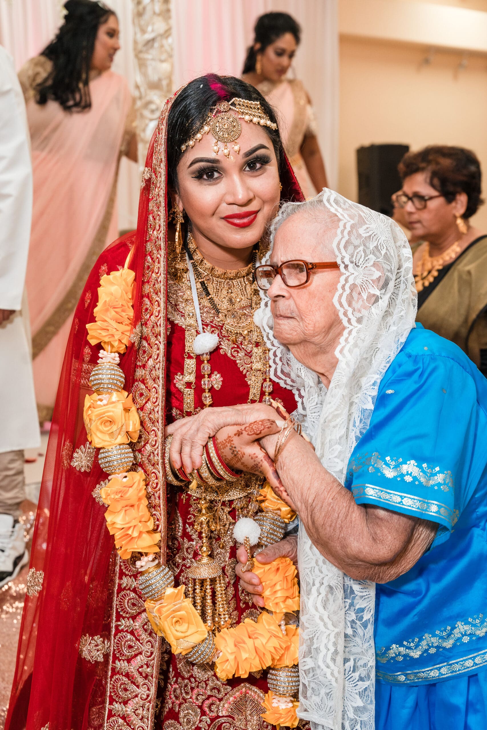 Bride wearing traditional cultural attire stands affectionately with her grandmother, sharing a moment of love and heritage