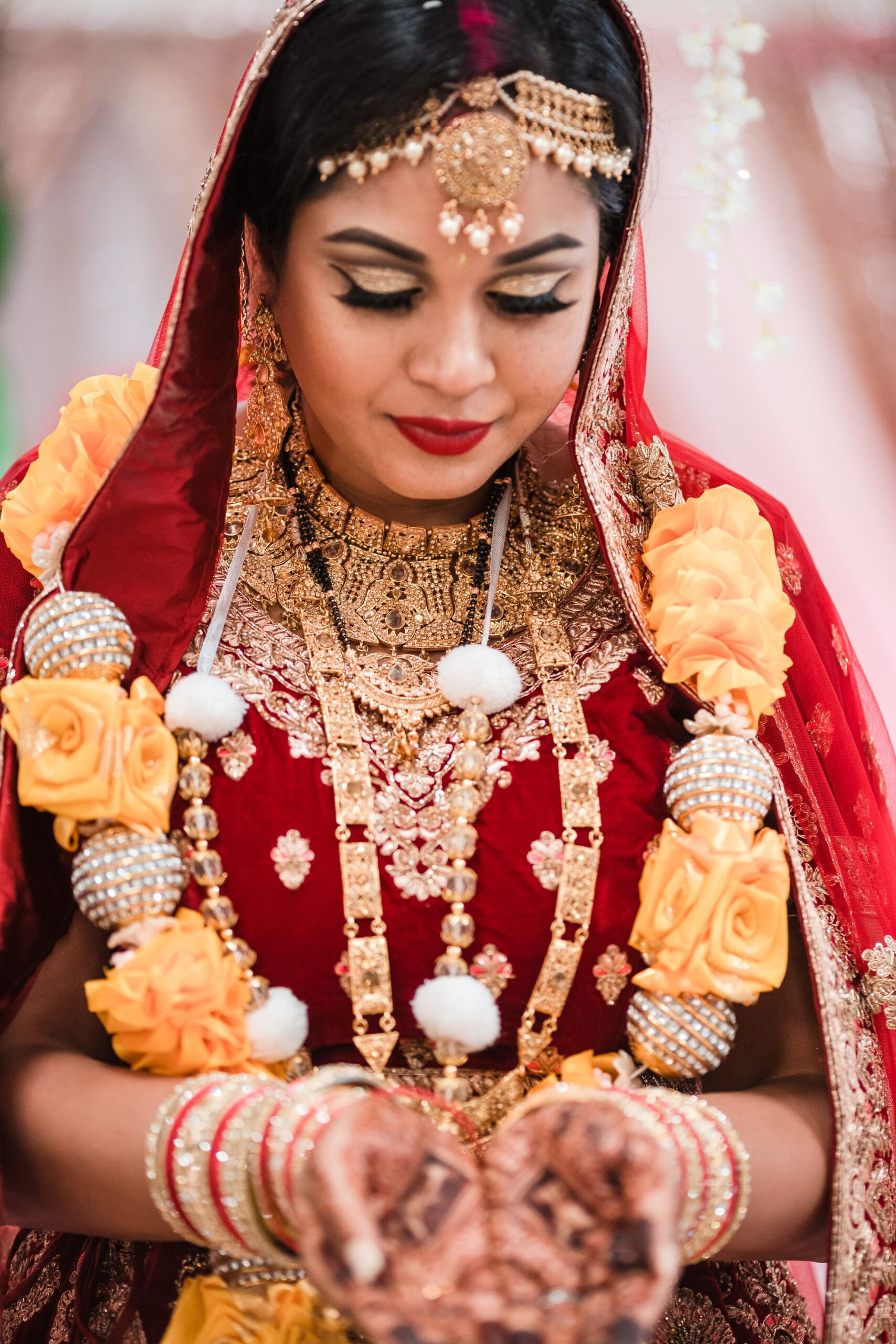 Solo portrait of the bride showcasing intricate henna designs on her hands, complementing her red and gold dress.