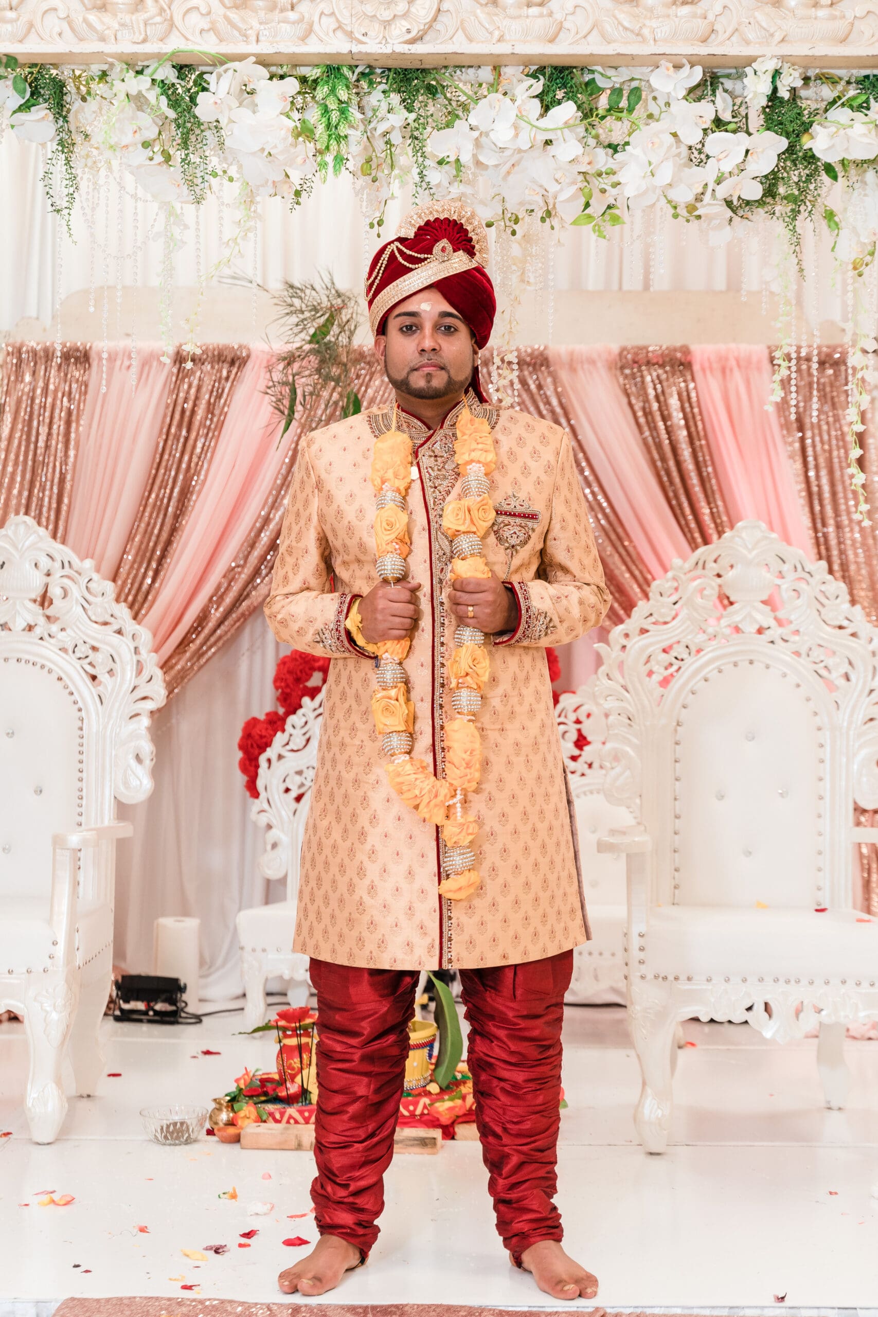 Solo portrait of the groom in traditional Indian wedding attire, featuring a vibrant red and gold outfit