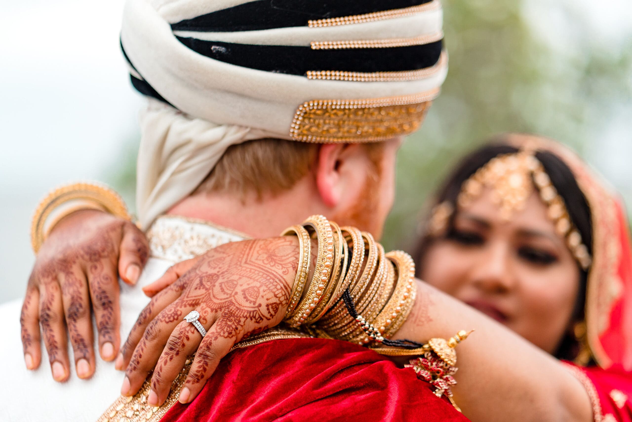 Close-up of newlyweds dancing in a cultural wedding ceremony, bride's hands adorned with henna tattoos and wedding ring.