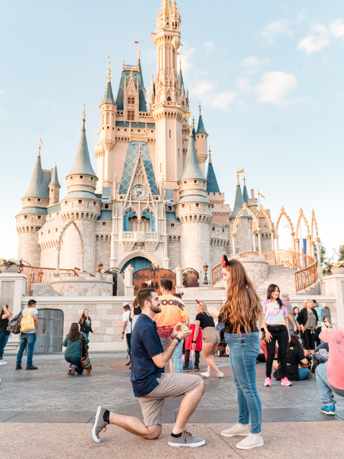 A man on one knee proposing to his partner with the Magic Kingdom castle in the background, captured by Jerzy Nieves in this unforgettable proposal photoshoot.