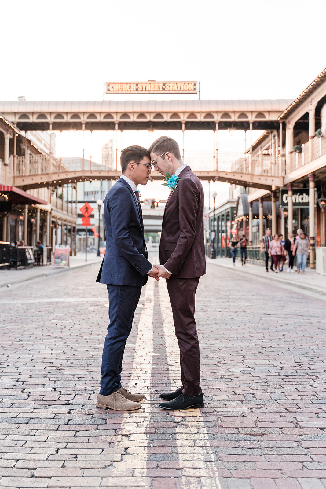 Two grooms touch foreheads under the iconic Church Street Station sign in downtown Orlando, FL, sharing a moment of love and connection.