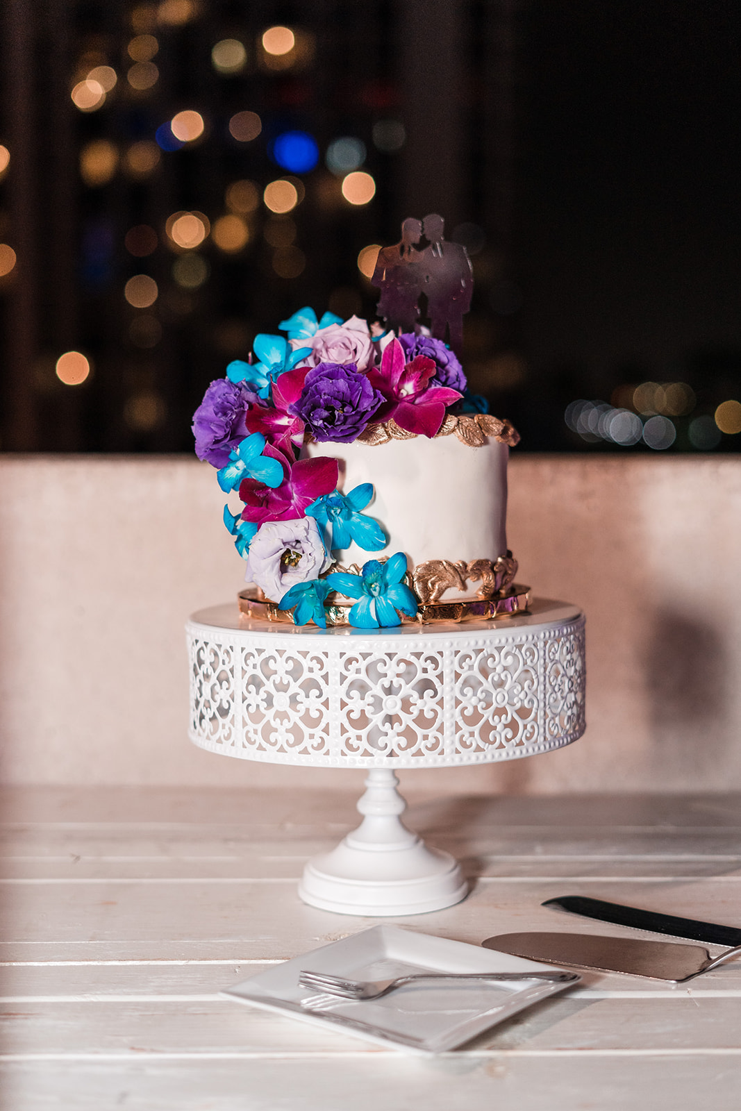 A modern wedding cake adorned with beautiful edible flowers, featuring a miniature figurine of the grooms on the top tier.