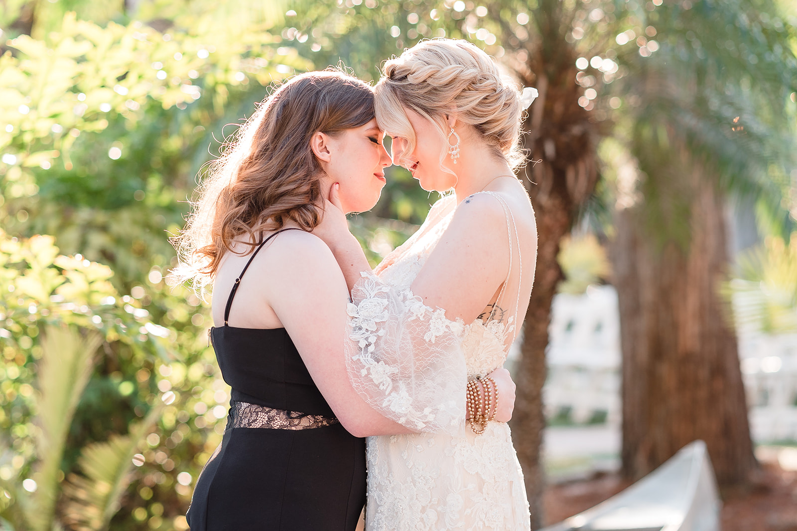 Two brides embrace each other tenderly against a backdrop of nature, their love illuminated by the serene beauty of the surroundings.