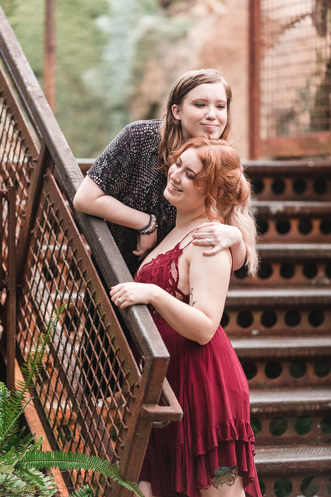 Two brides embrace on a stairwell, one resting her head on top of the other's head, capturing a moment of love and affection in this unique photo opportunity.