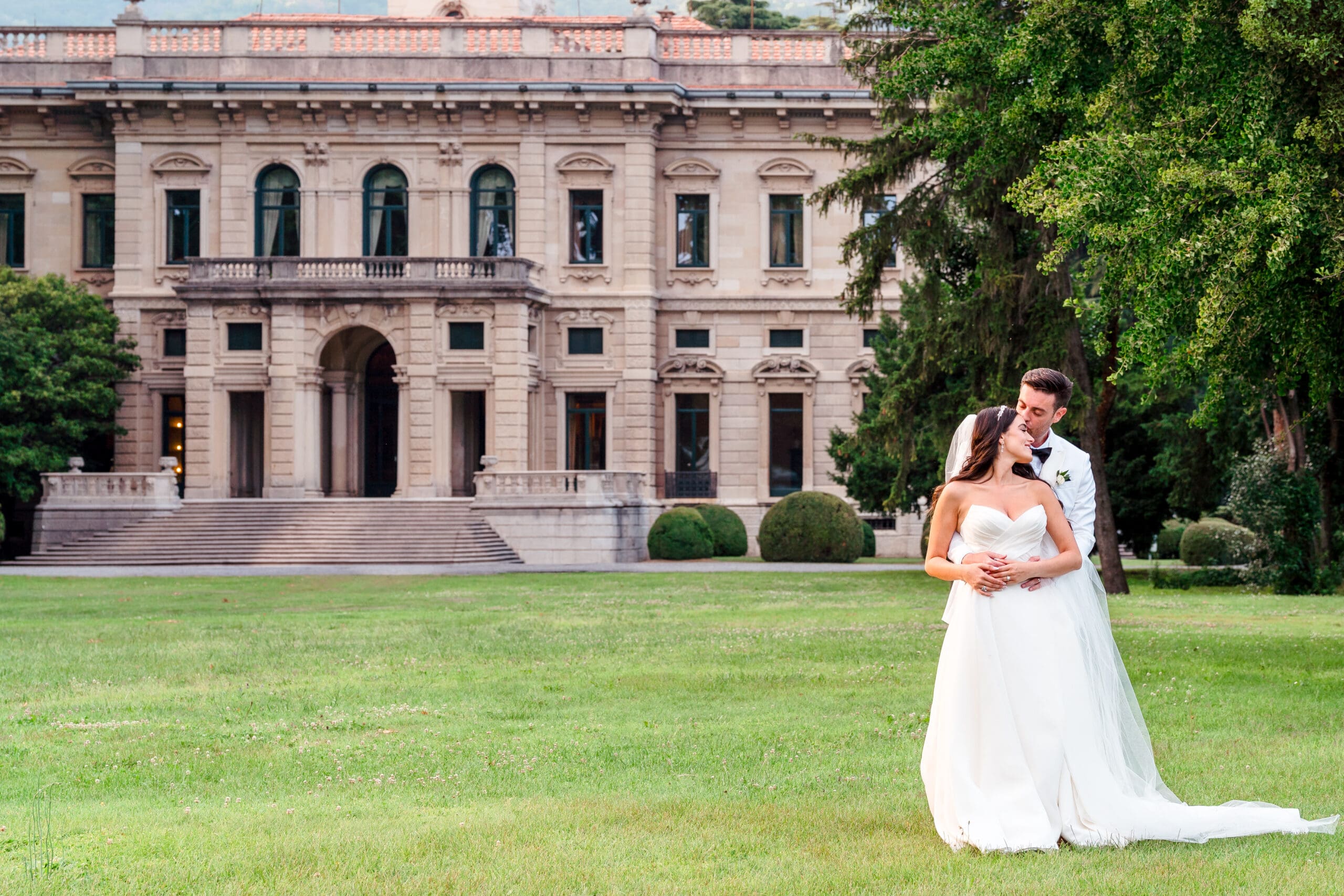 Captivating destination wedding moment: Couple stands in front of the mansion at Lake Como wedding in Italy, with Villa Erba in the background, creating a picturesque scene filled with elegance and romance.