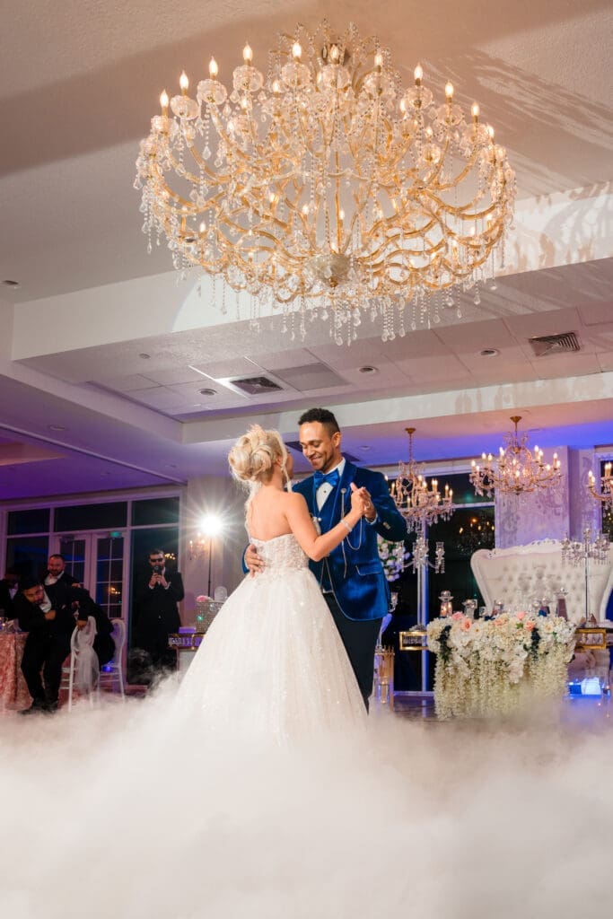 Elegant wedding reception scene with dancing couple, showcasing beautiful dance floor and chandelier, enhanced by elegant fog, capturing class and romance.