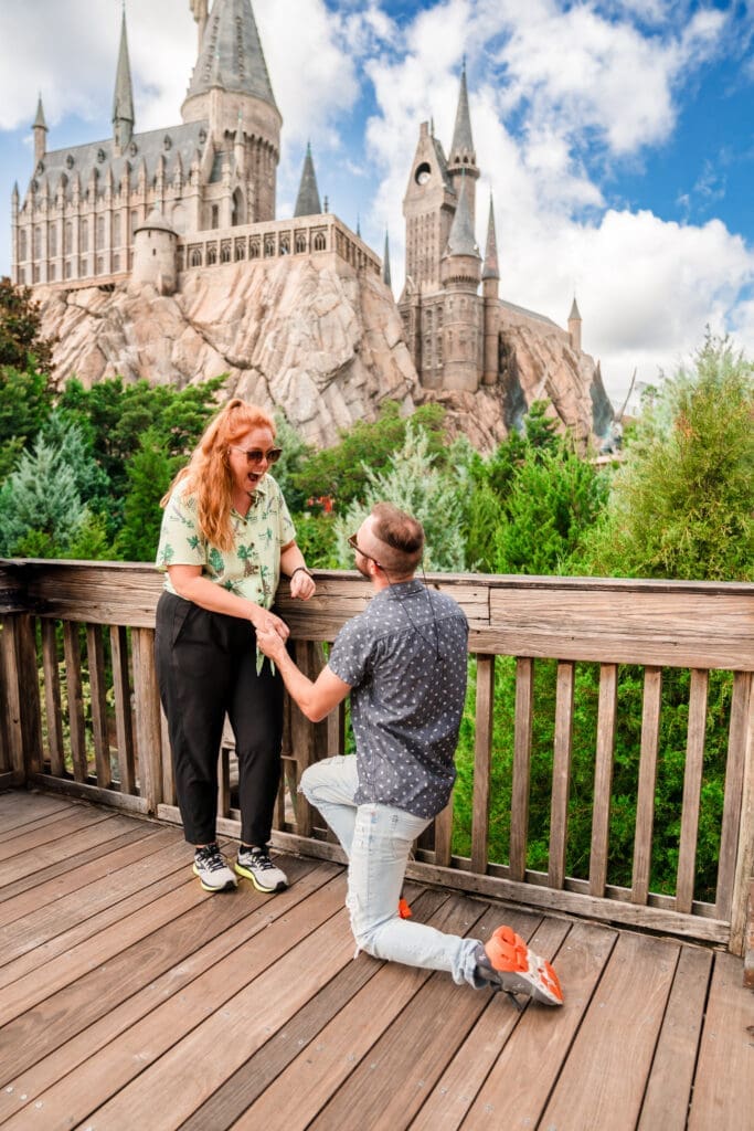 Captivating proposal moment: Girl in shock with her jaw dropped as he gets on his knee to ask the question, with the Disney castle in the background, creating an amazing photo shoot.
