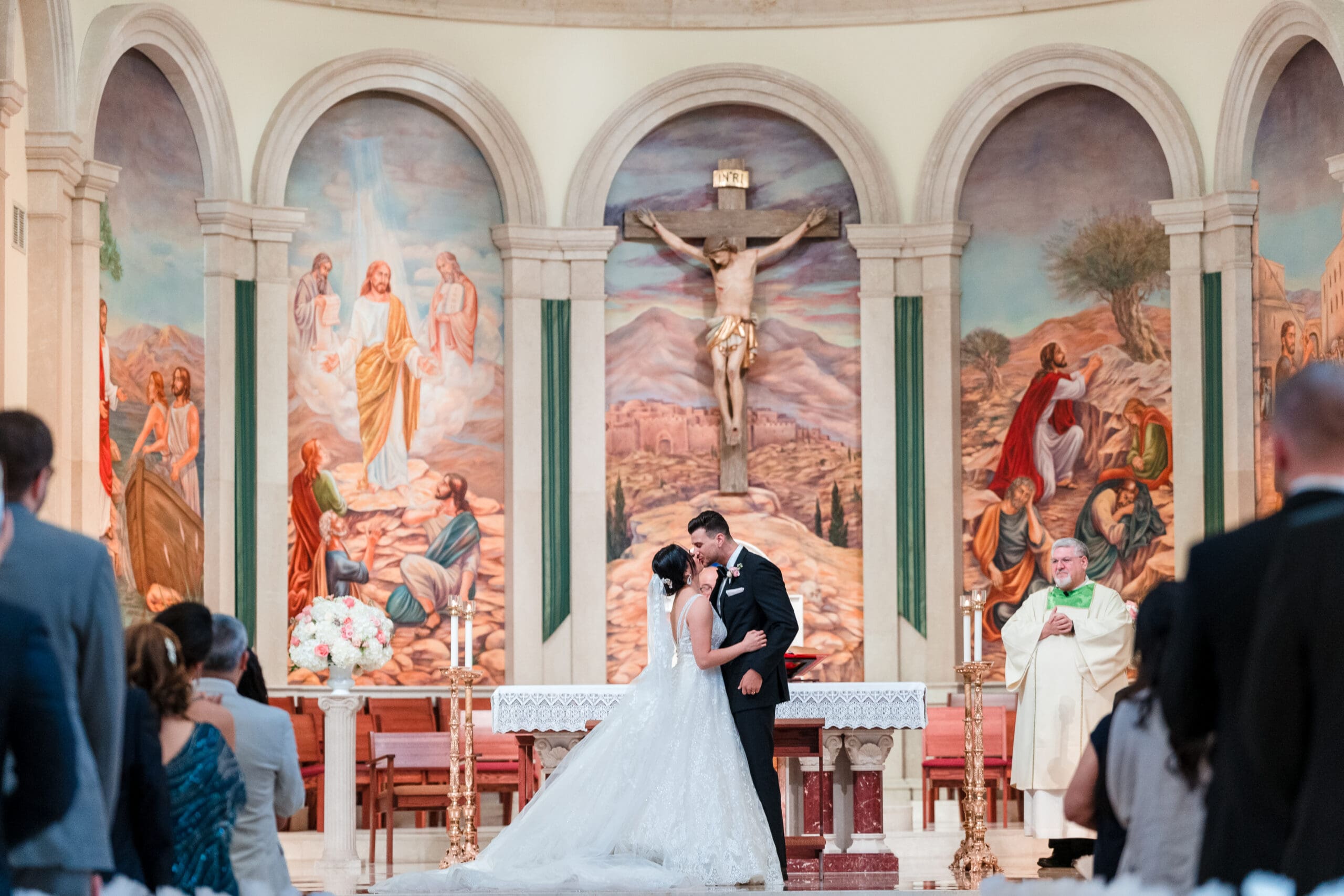 A beautiful chapel scene with a painting in the background, capturing the bride and groom kissing at the altar.