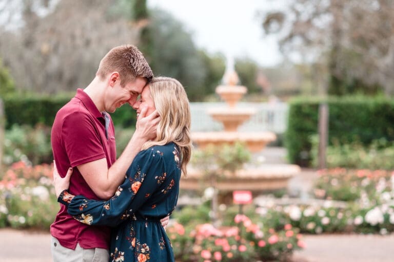 Engagement photo of couple in front of fountain, touching foreheads and noses with huge smiles, showing their unique love and connection.