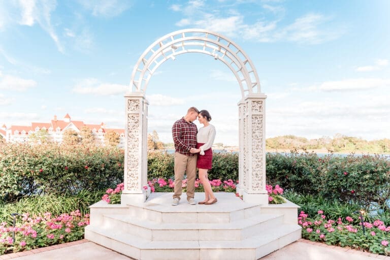 Engagement photo at Disney, with the couple standing at the altar before their wedding during an engagement shoot, touching foreheads in embrace under the archway of the outdoor wedding area, with the lake in the background at this Disney venue.