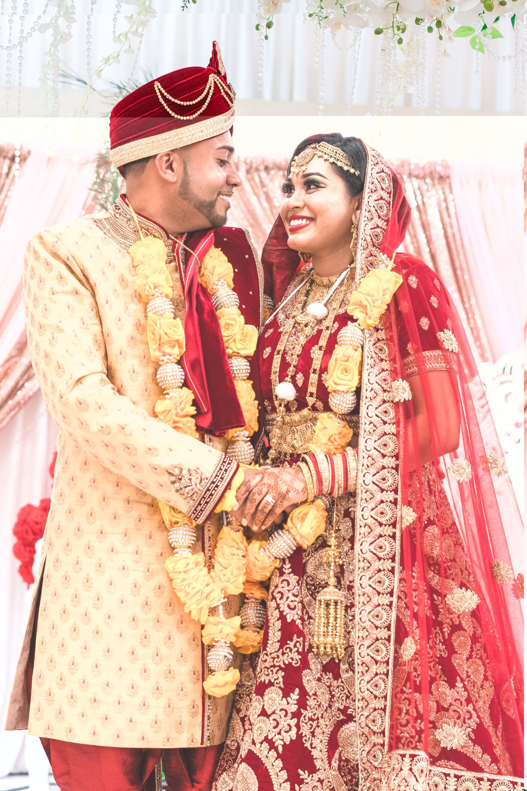 A couple dressed in red and gold traditional Indian wedding garments gaze into each other's eyes, embodying love and cultural richness.